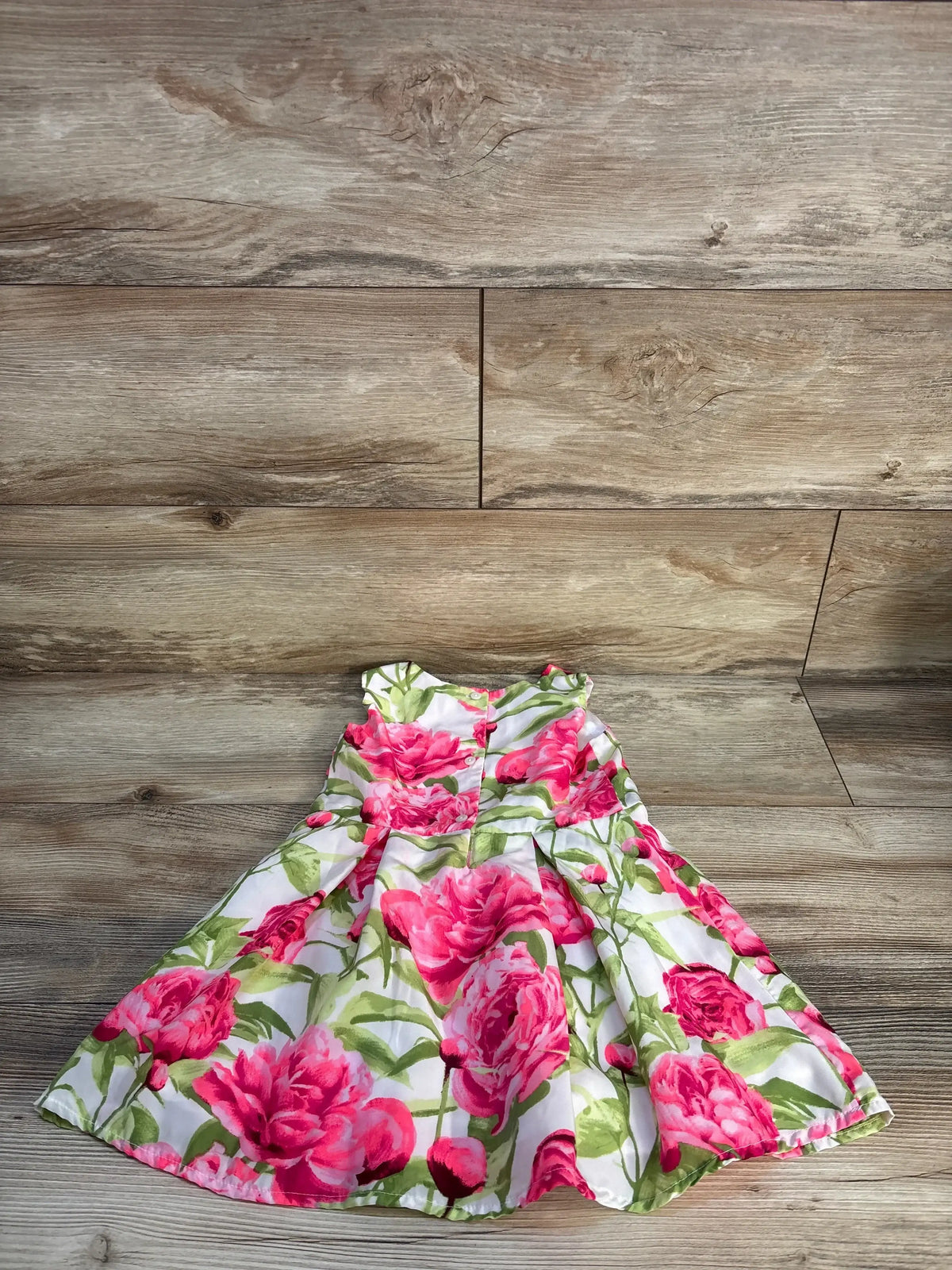 Girls floral dress with pink and green rose pattern on wooden floor background