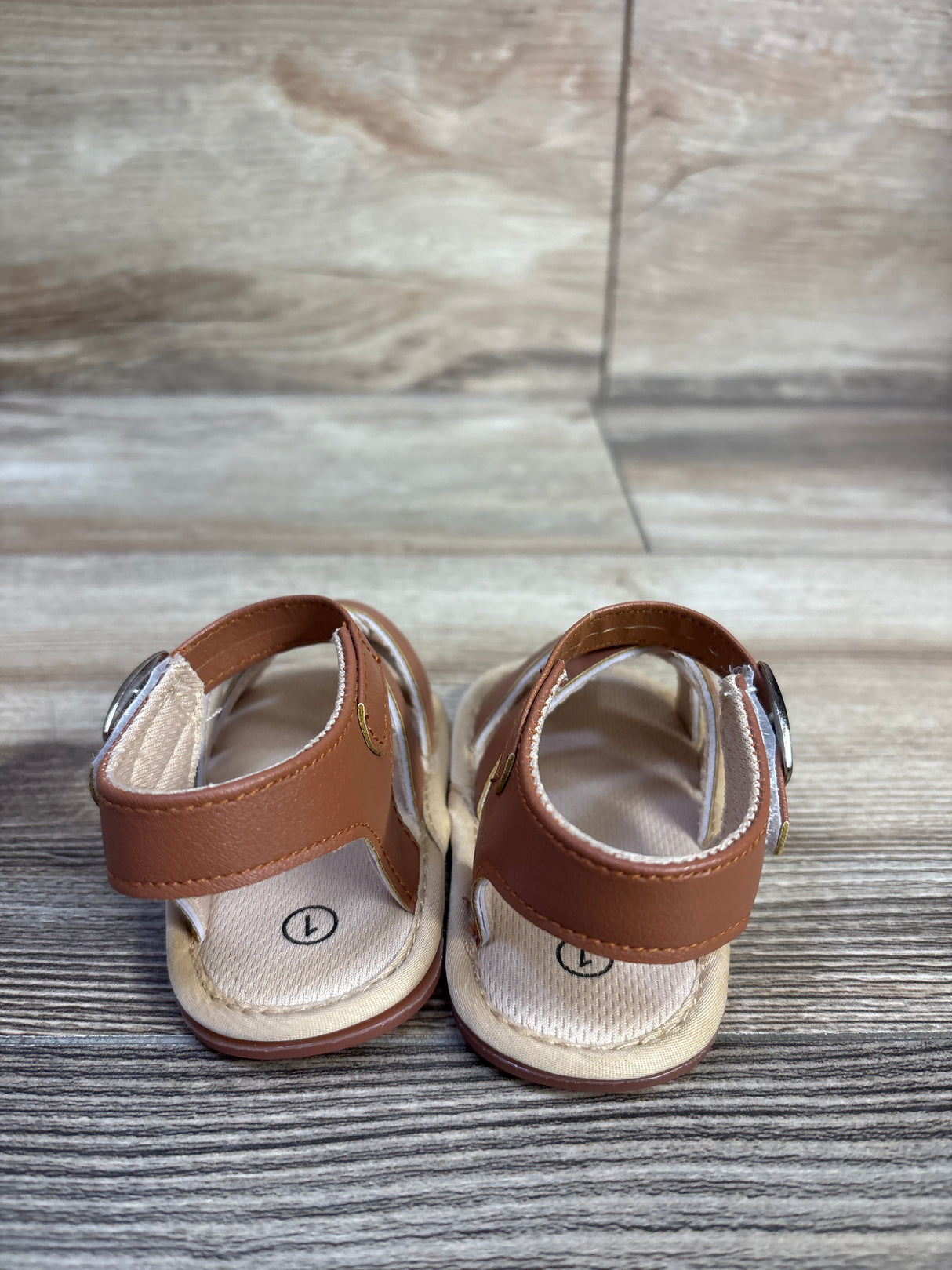 Rear view of Hsdsbebe brown soft-sole baby sandals with Velcro ankle straps and cushioned fabric insoles on wood background