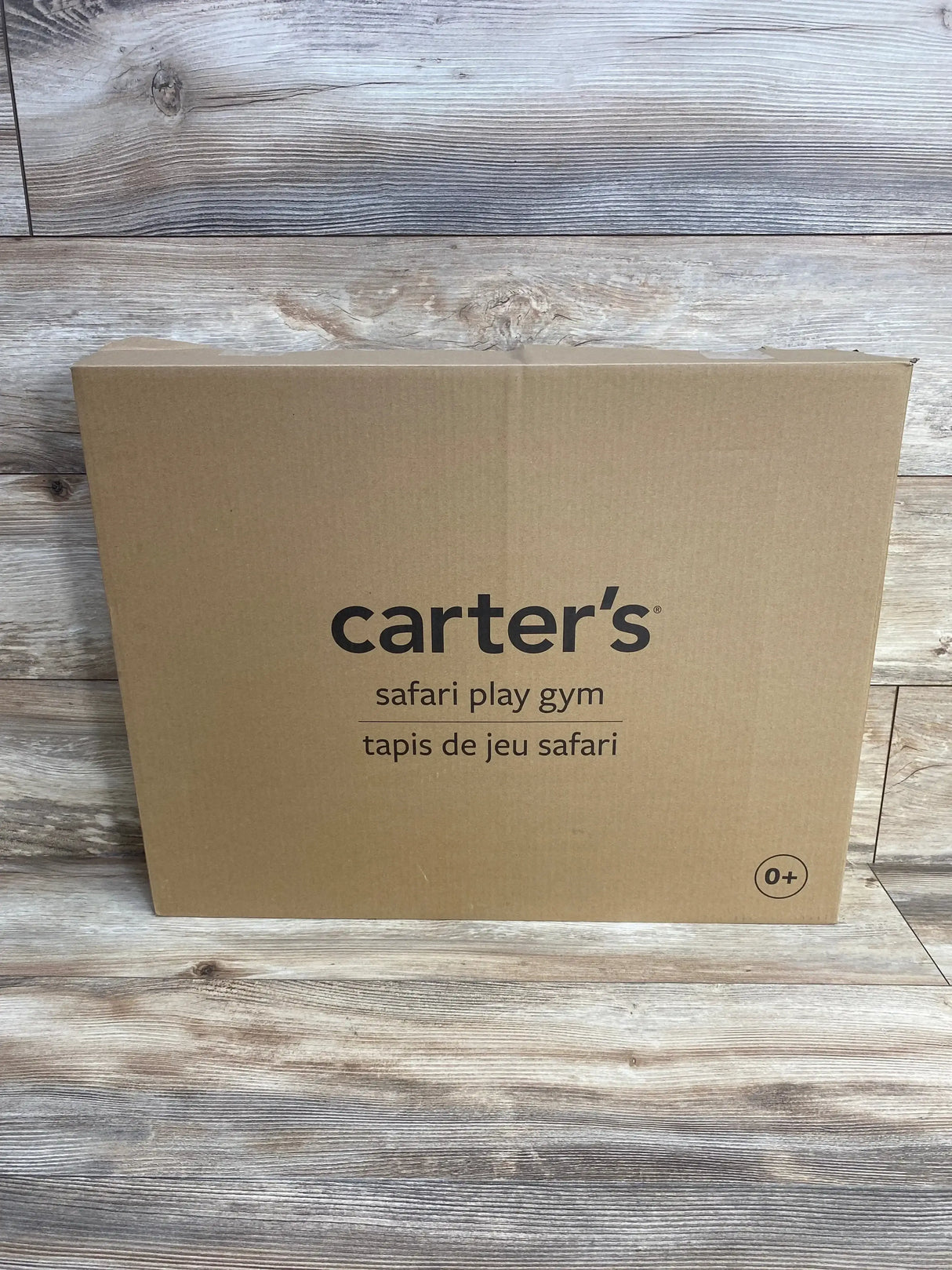 Front of Carter’s Safari Play Gym cardboard box showing brand name and product label on a wood plank background