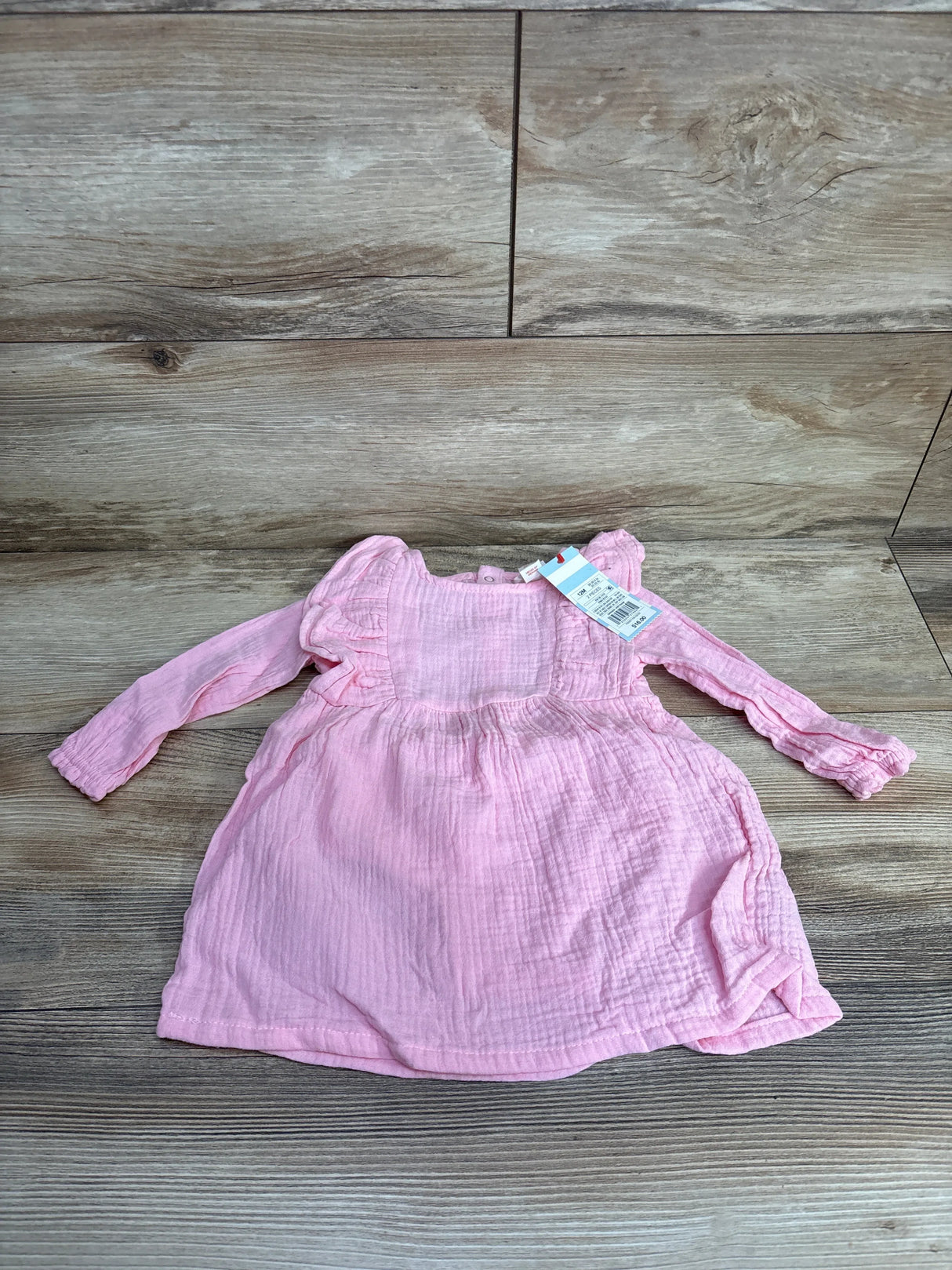 Pink long sleeve baby dress with ruffle shoulders on wood background, gently used kids clothing