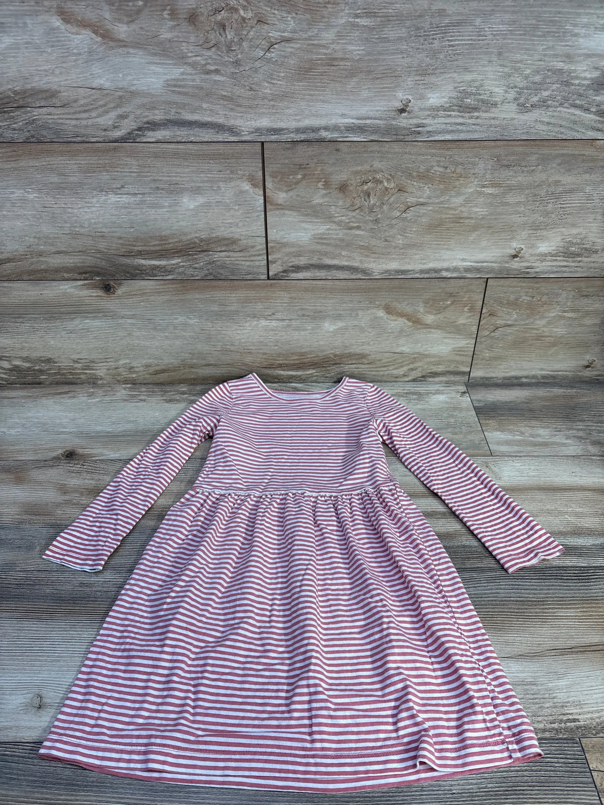 Front view of Carter’s long sleeve striped dress showcasing pink and white stripes with a wood-look floor background