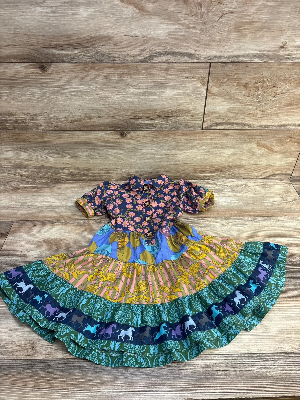 Flat lay of Matilda Jane 2T dress with navy floral bodice and multicolor tiered skirt featuring horse trim on wood background