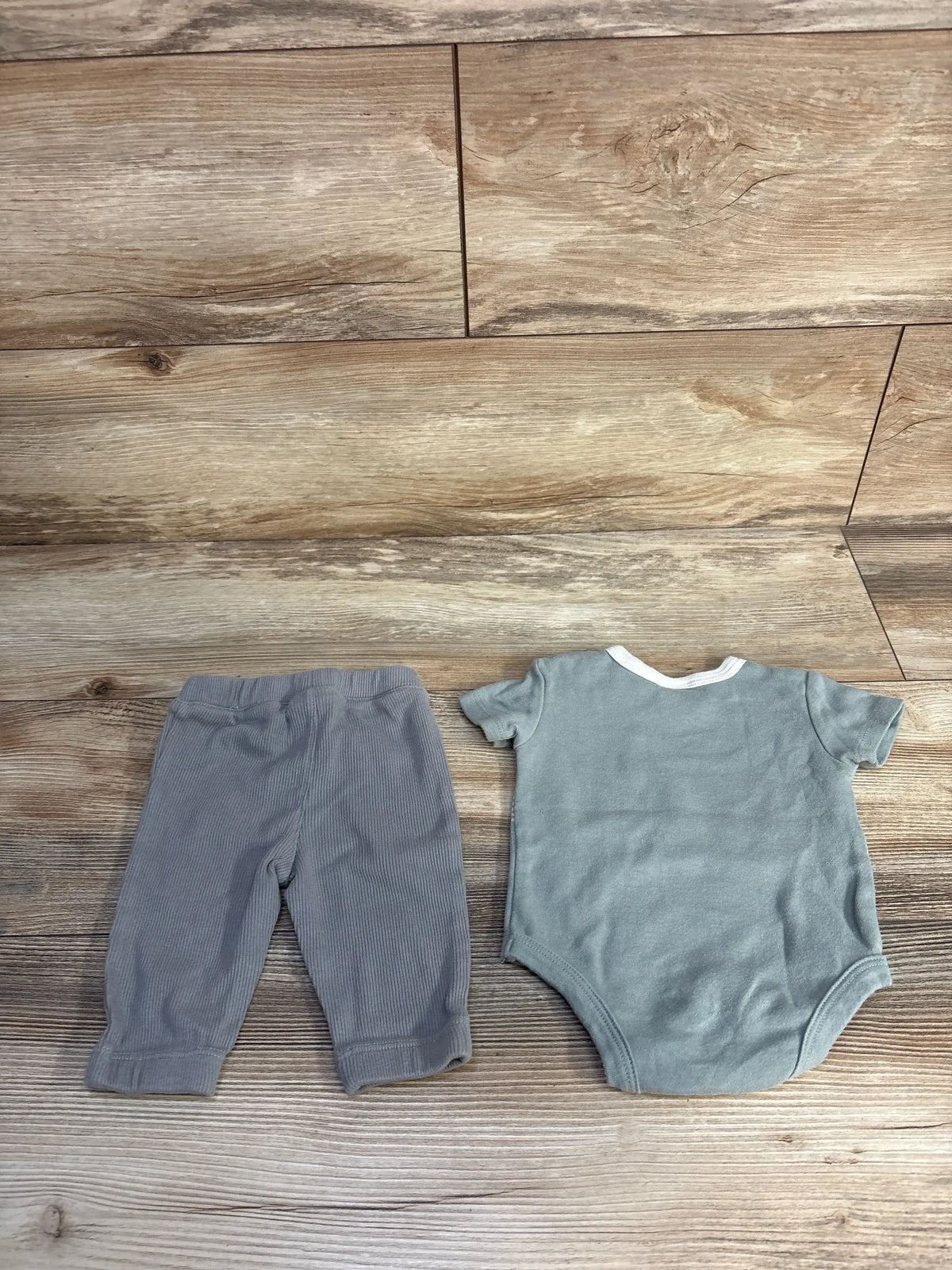 Top view of Mario Lopez green bodysuit and pants set, size 0/3 months, showing coordinated pieces on wood-look flooring