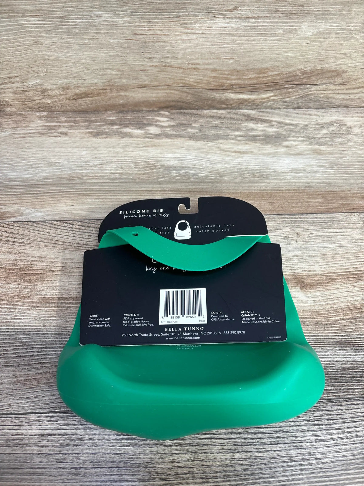 Green silicone baby bib with adjustable neck and catch pocket on wooden surface
