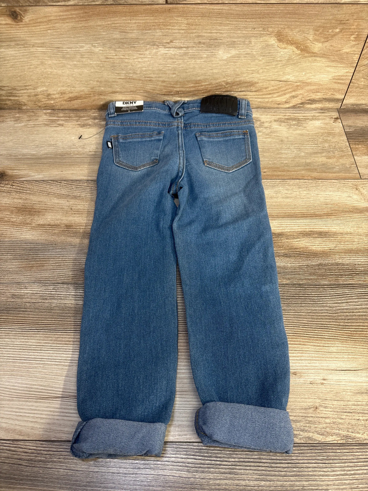 Back view of NEW DKNY distressed jeans, blue size 5T, showcasing back pockets and rolled cuffs on wood-grain flooring