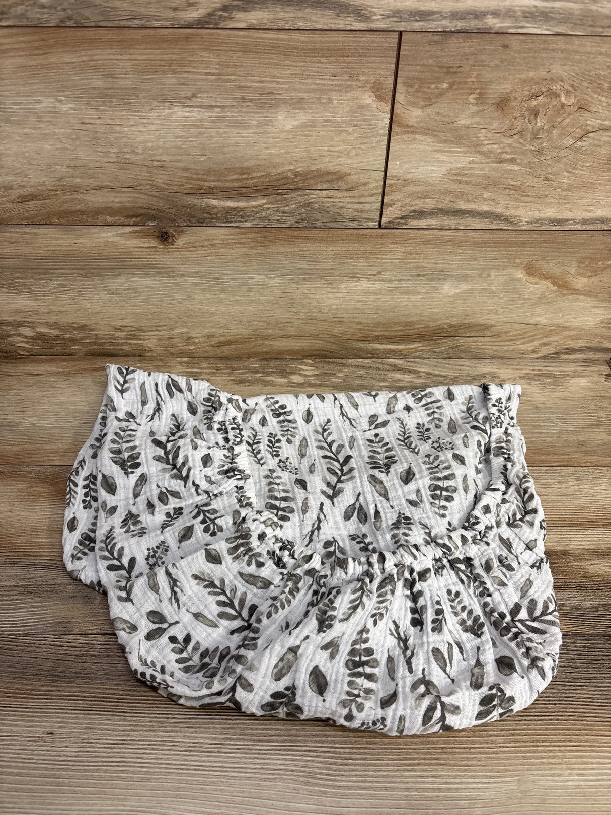 White and gray floral fitted crib sheet on wood floor