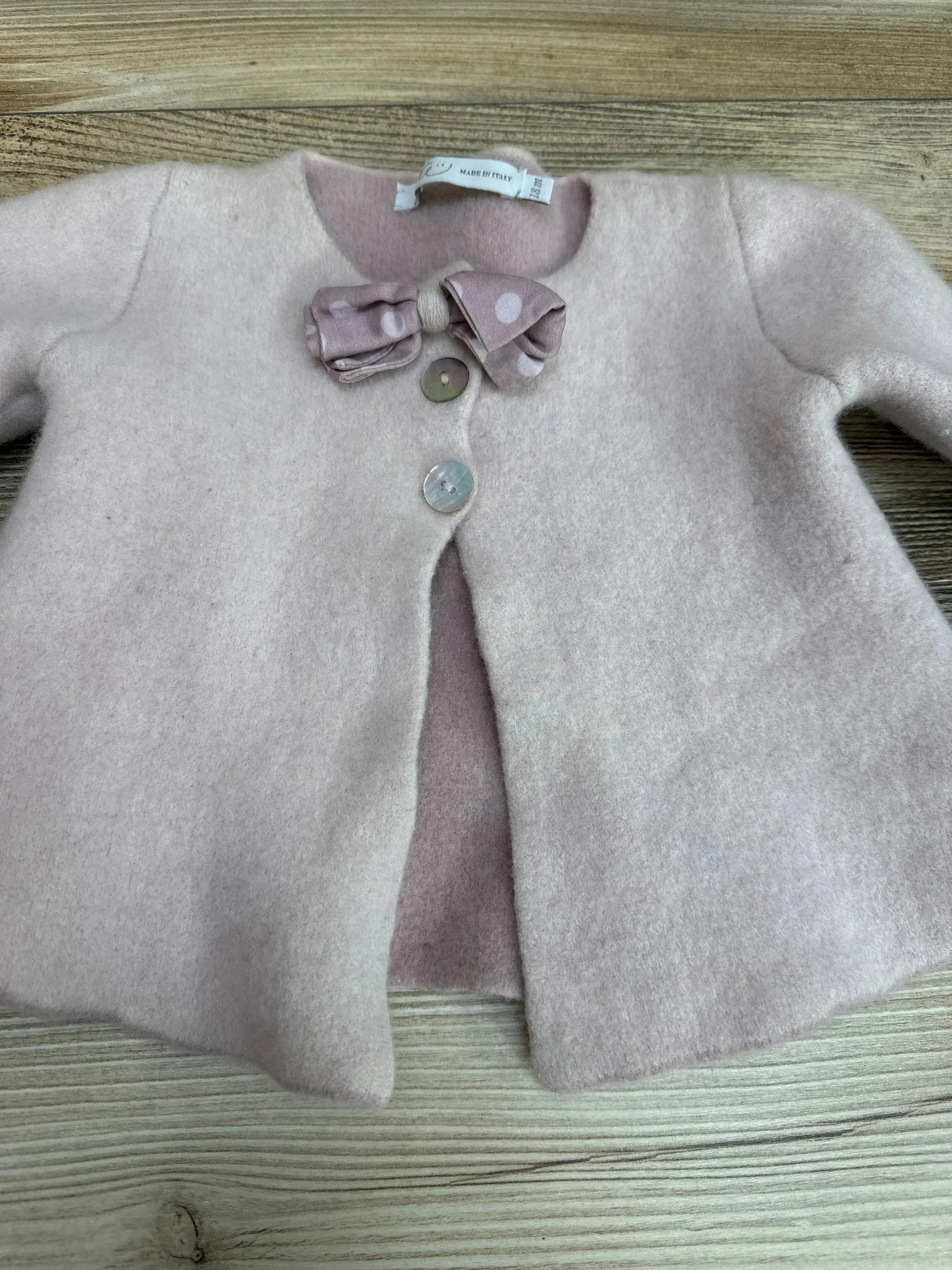 Top-down view of baby girl pink cardigan (18M) showcasing three shell buttons and a polka-dot bow on a light wood background