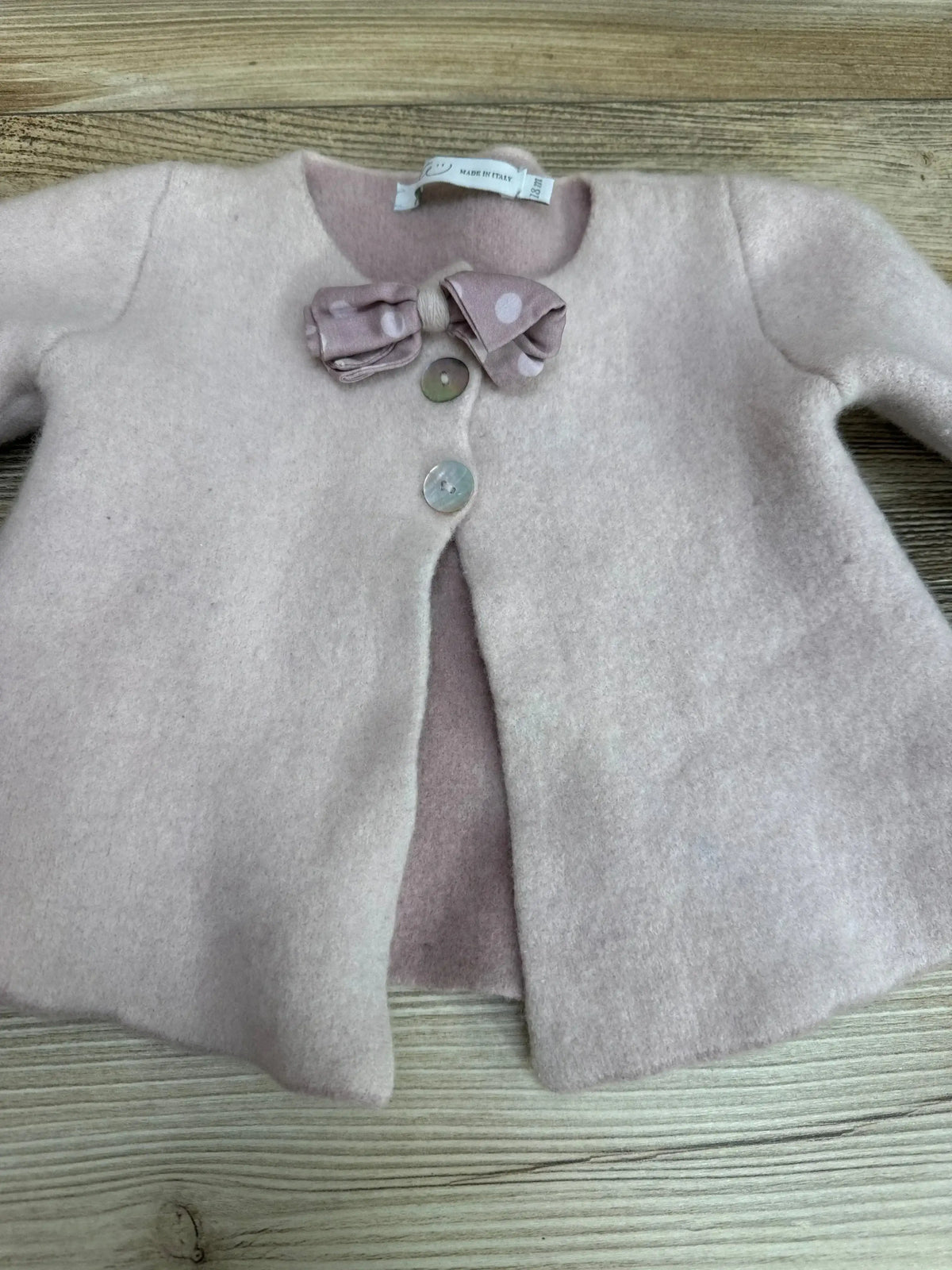 Top-down view of baby girl pink cardigan (18M) showcasing three shell buttons and a polka-dot bow on a light wood background