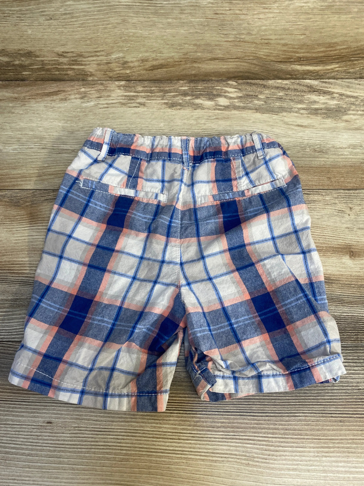 Plaid toddler boys shorts with blue, white, and peach check pattern on wood background