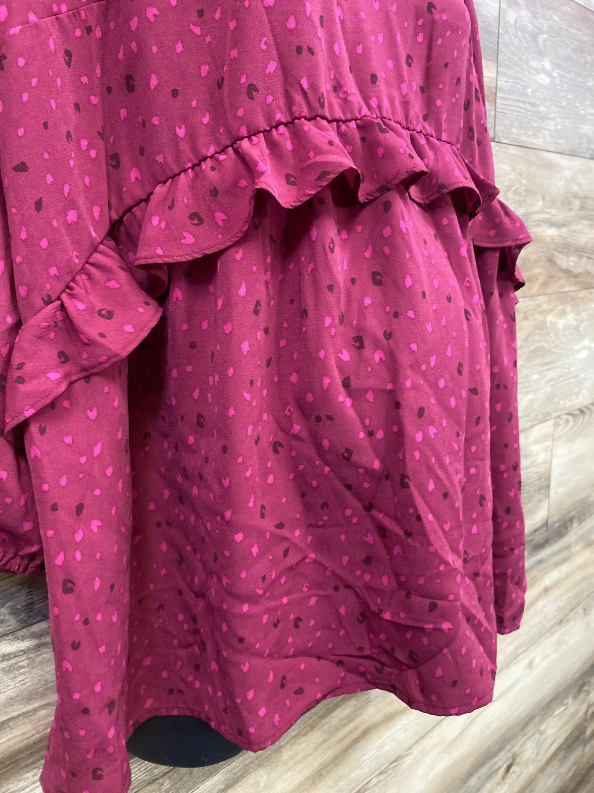 Close-up of ruffle-waist maternity woven top showcasing ruffle trim and pink speckled berry print against wood floor background