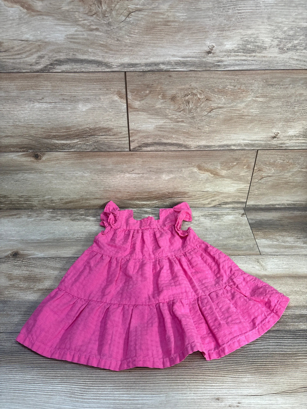 Front view of Old Navy pink smocked tiered dress size 12 to 18 months with tiered skirt on gray wood floor