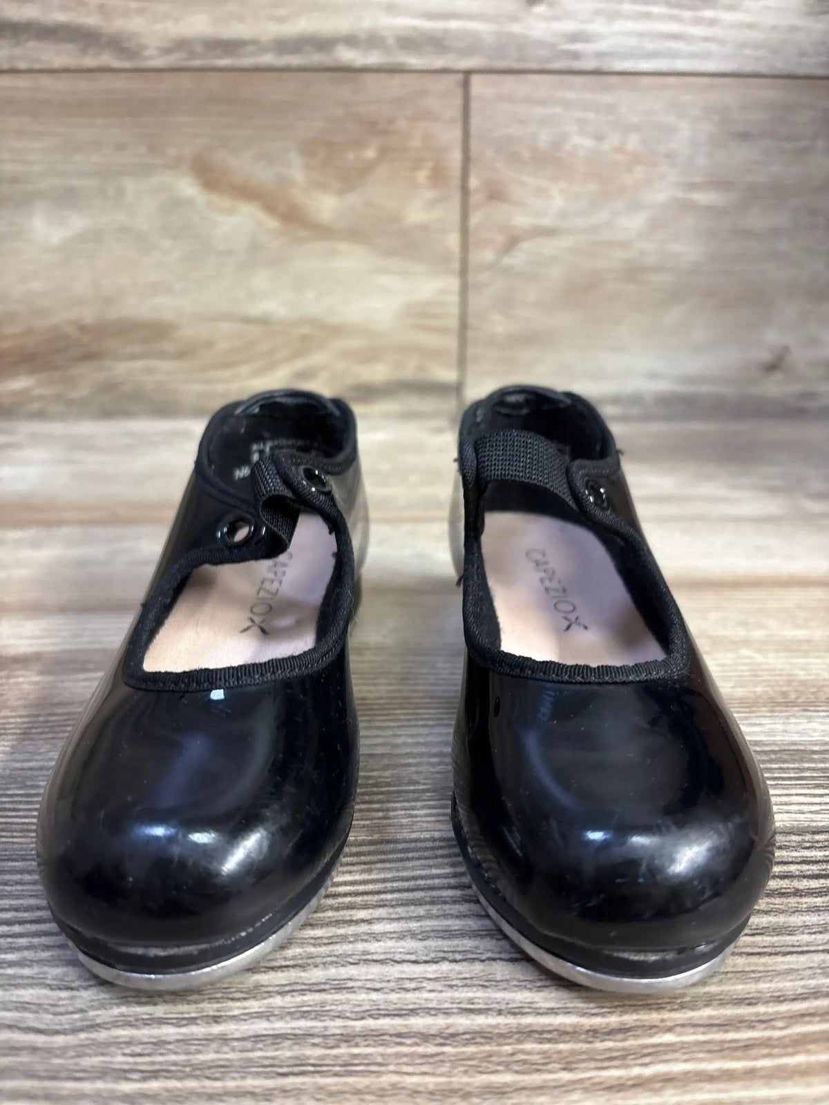 Black patent leather child tap shoes with elastic straps on wood floor