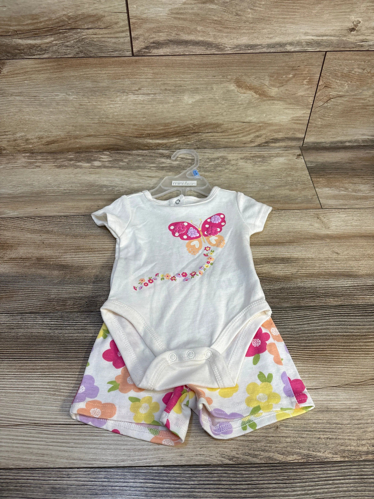 White baby onesie with pink butterfly and floral shorts, mini bean brand on hanger