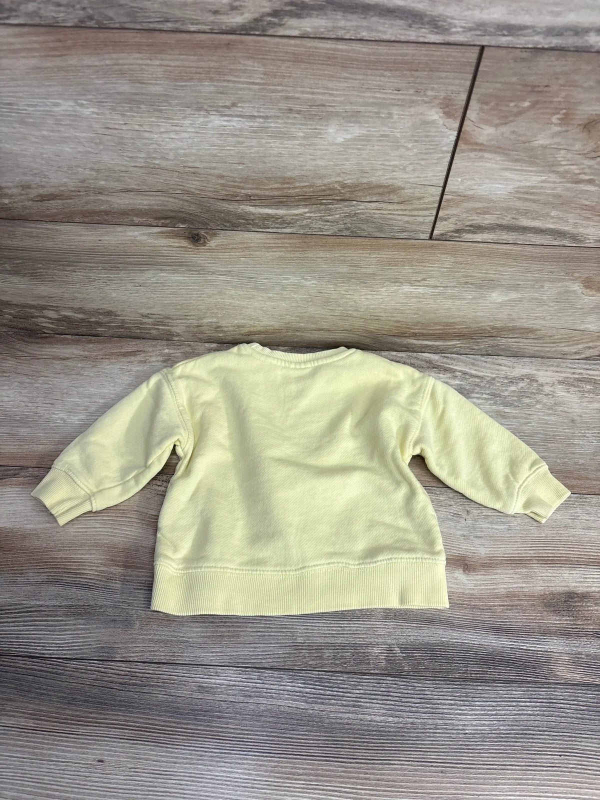Light yellow long sleeve toddler sweatshirt on wood background, gently used kids clothing