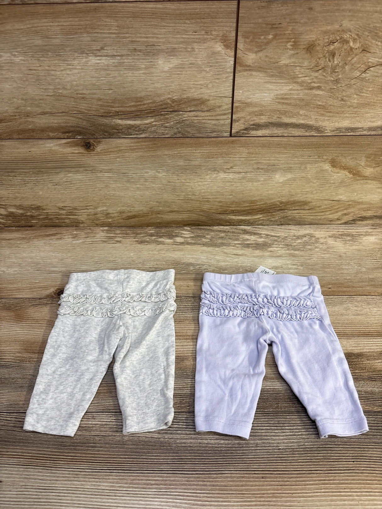 Back view of two baby ruffle pants, lavender and heather gray, showing three ruffle tiers across waist on a wood background