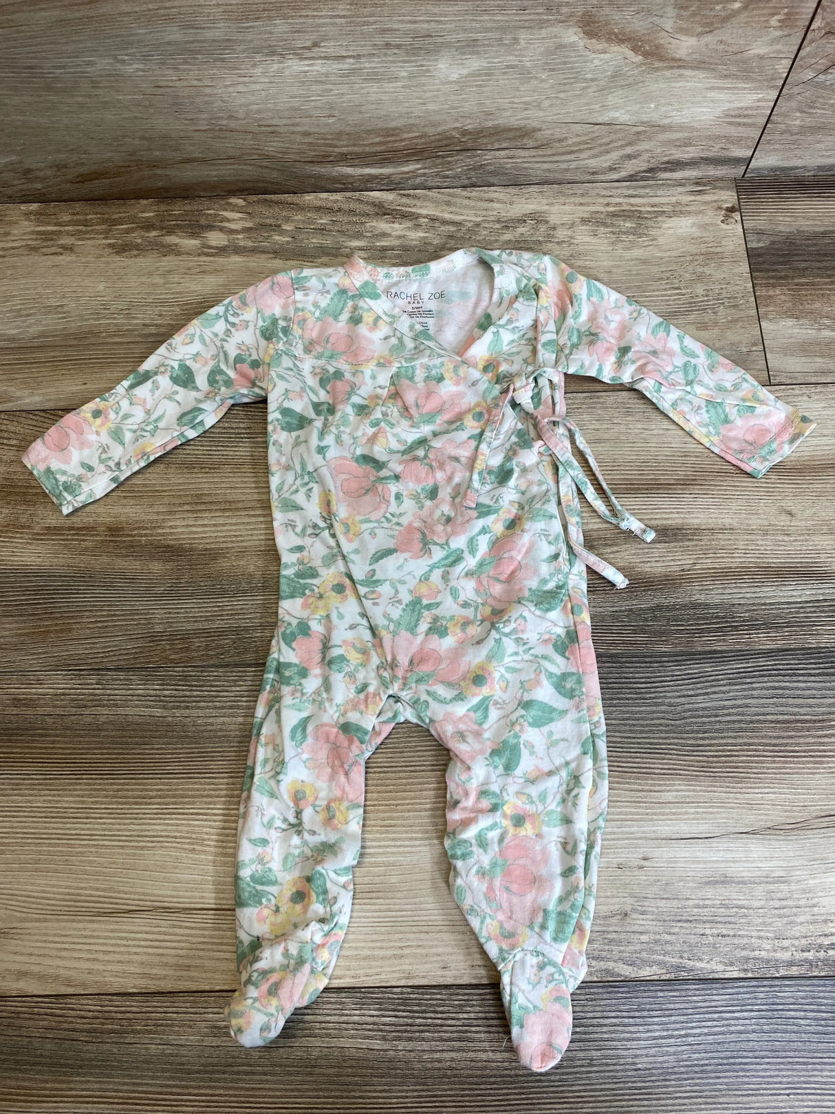 Flat lay of Rachel Zoe floral footed coverall, 6-9 months, showing side tie, long sleeves, and footed legs on wood floor