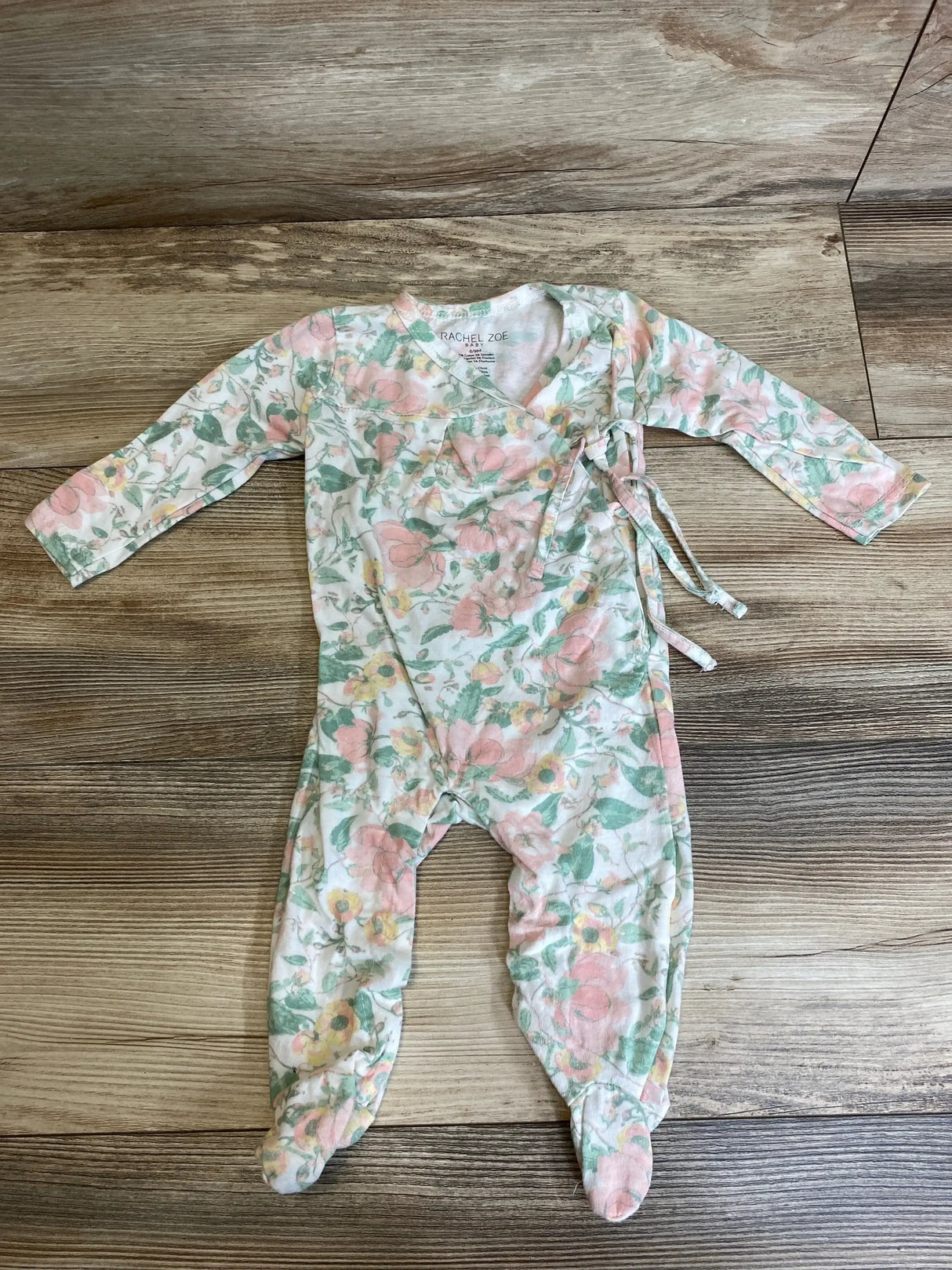 Flat lay of Rachel Zoe floral footed coverall, 6-9 months, showing side tie, long sleeves, and footed legs on wood floor