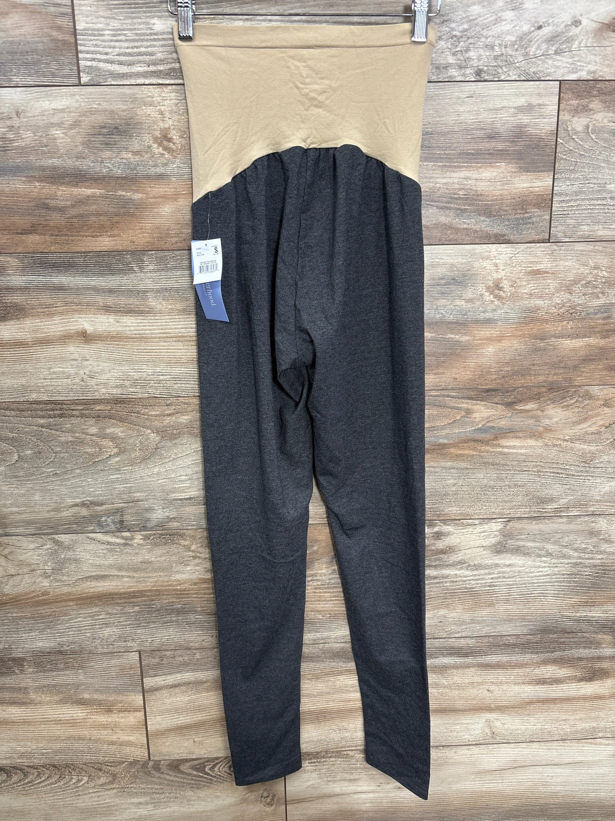 Maternity leggings with beige high waistband and dark gray legs hanging on wooden floor