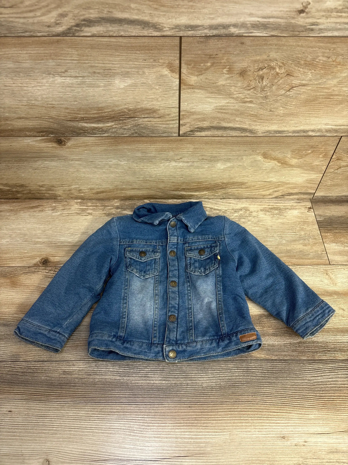 Blue denim toddler jacket with buttons and front pockets on wood floor background