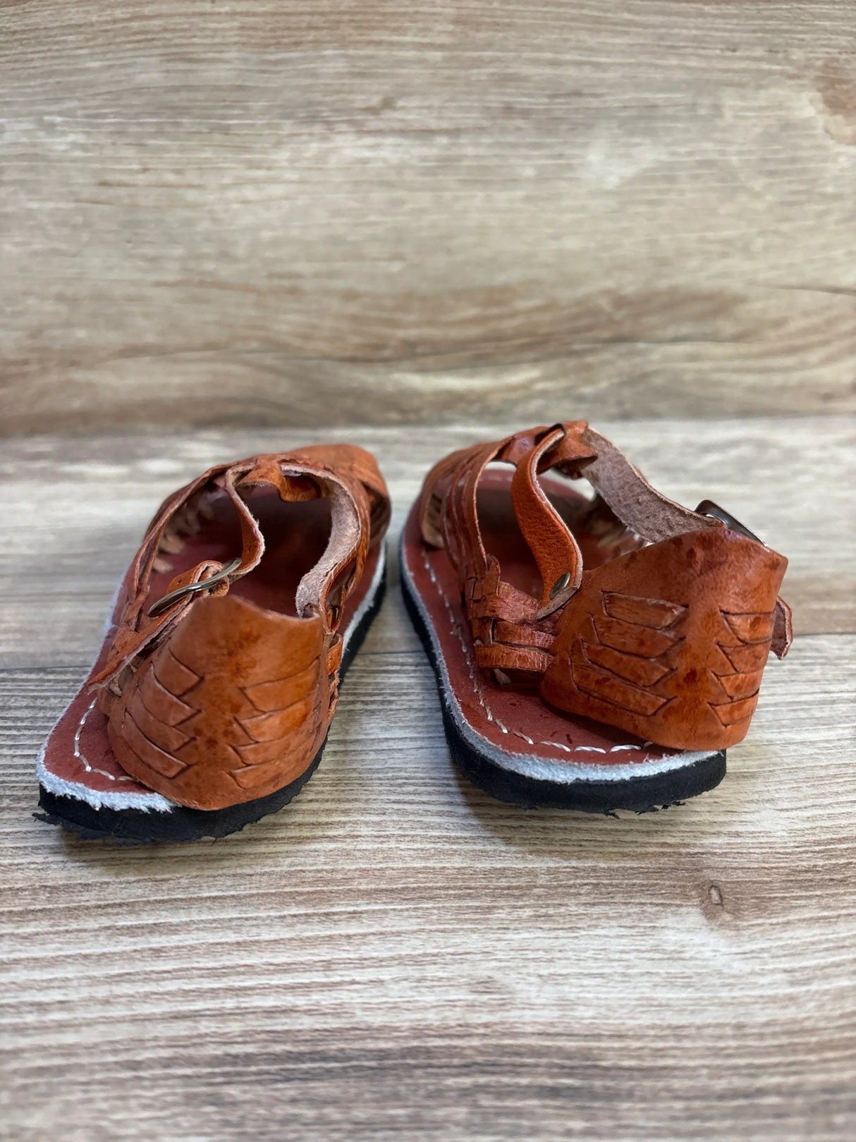 Brown leather kids' sandals with open heel, on wood background