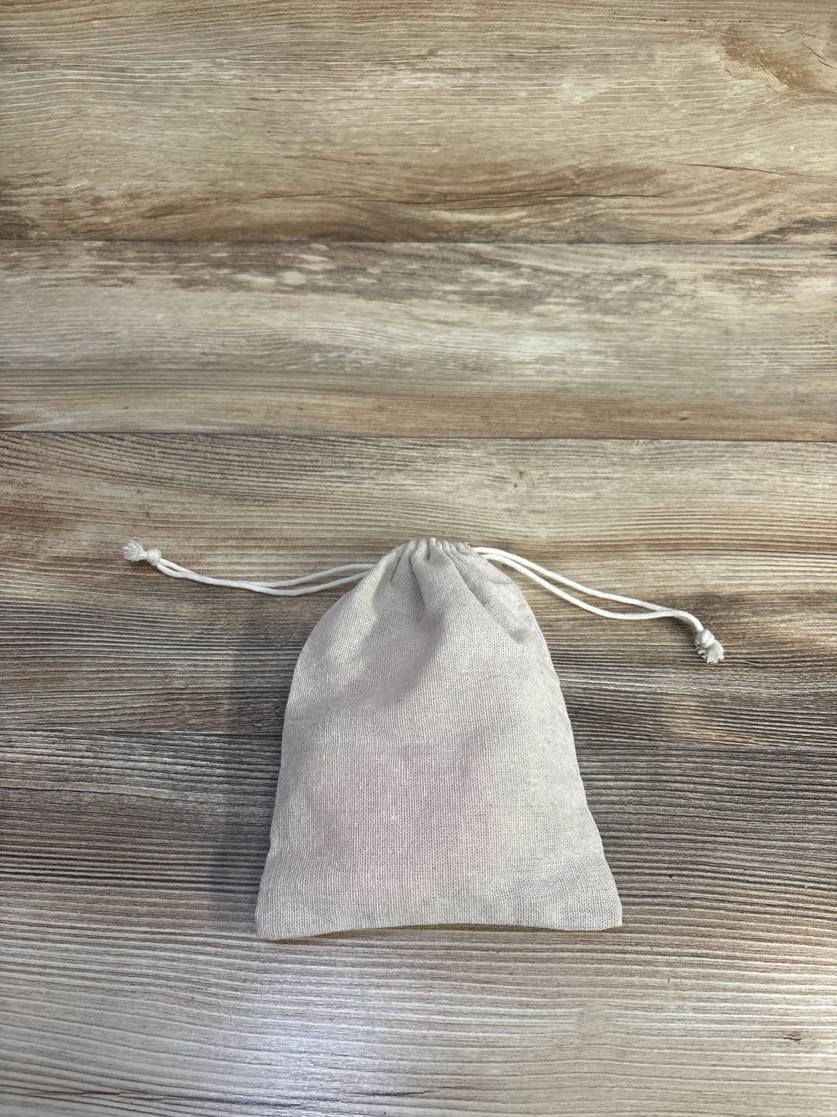 Top-down view of a beige drawstring pouch containing a 5-pack of pink baby mittens size 0-6 months on a wood surface
