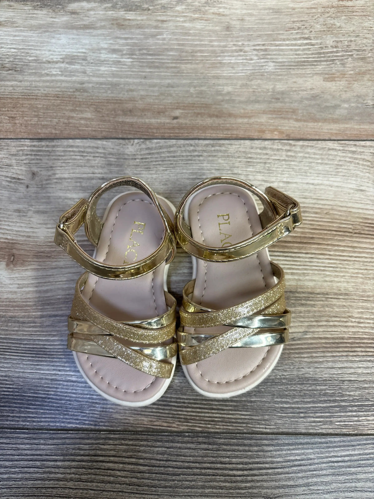 Children's Place glitter and metallic gold sandals for toddlers on a wooden background