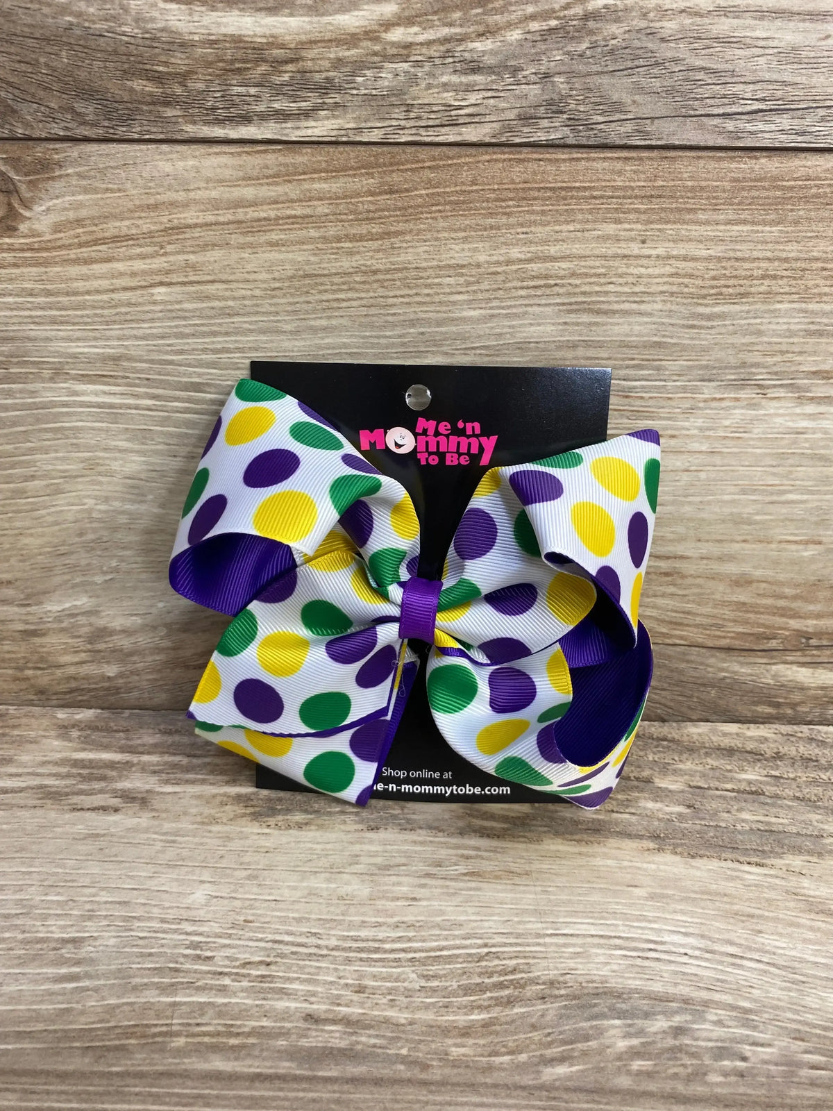 Front view of Mardi Gras polka-dot hair bow with white grosgrain ribbon and purple, green, yellow dots on wood background