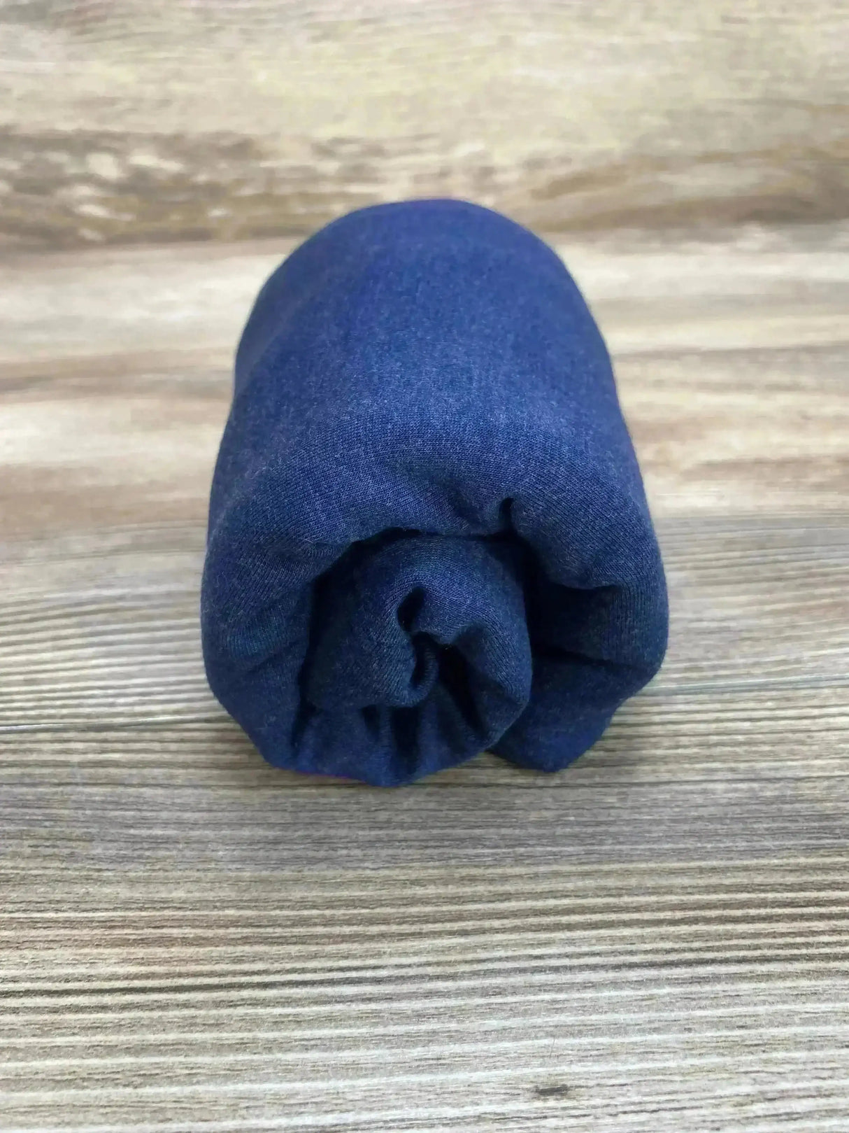 Front view of Jujube 6-in-1 car seat cover in navy showcasing rolled compact shape and fabric texture on wooden surface