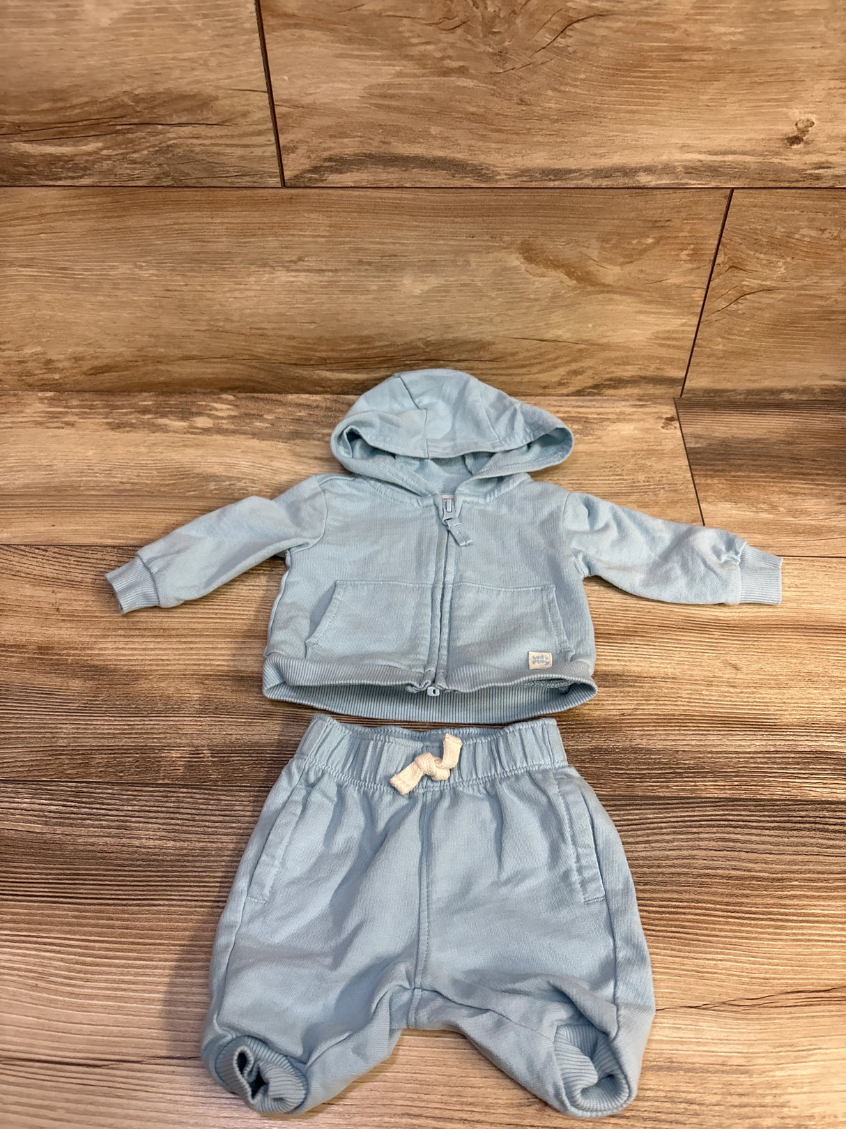 Flat lay of Carter’s light blue zip-up hoodie and pants set showing hood, front pockets, and drawstring waist on wood background