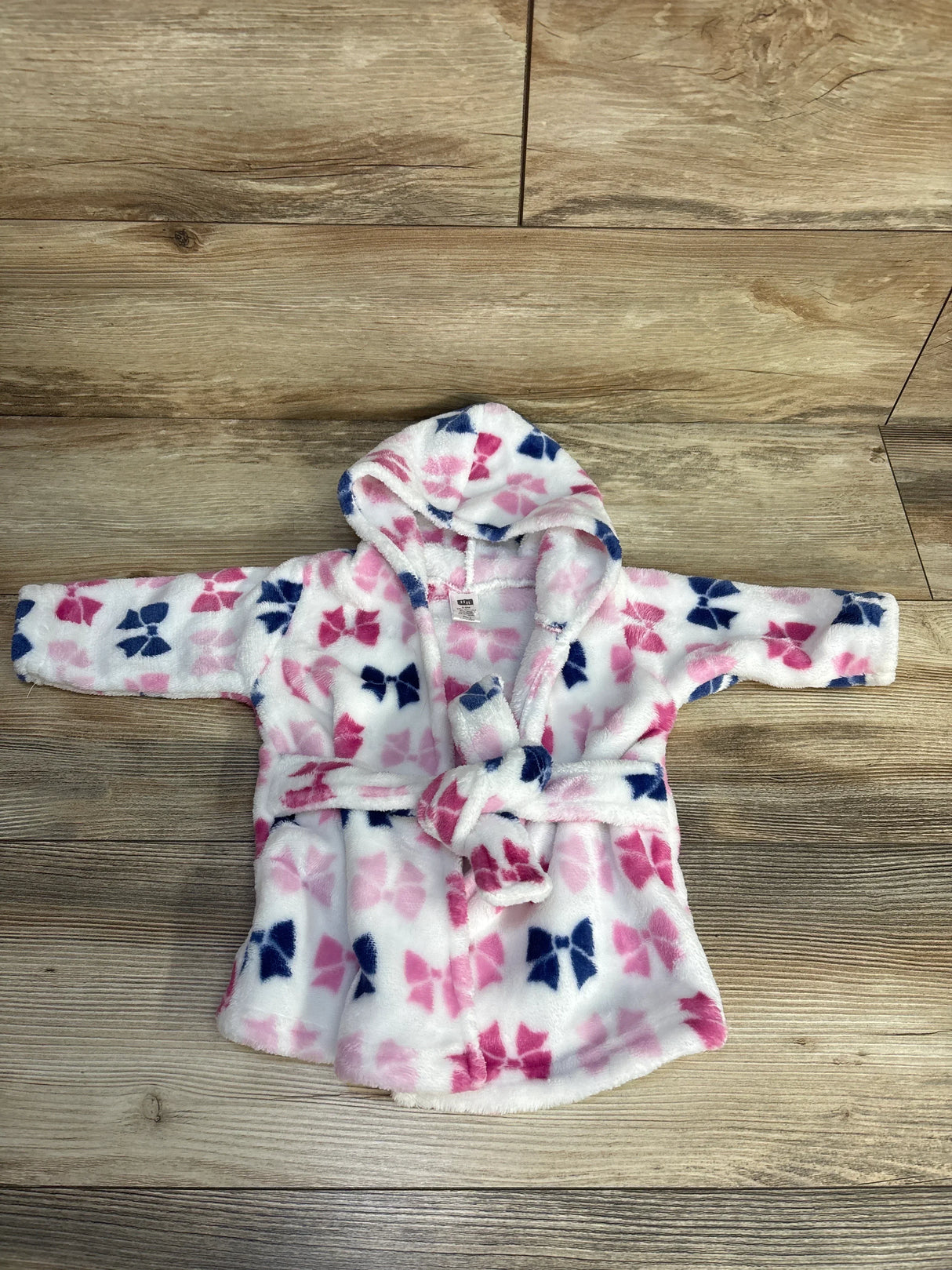 Plush baby bathrobe with pink and navy bow print and hood on wood floor