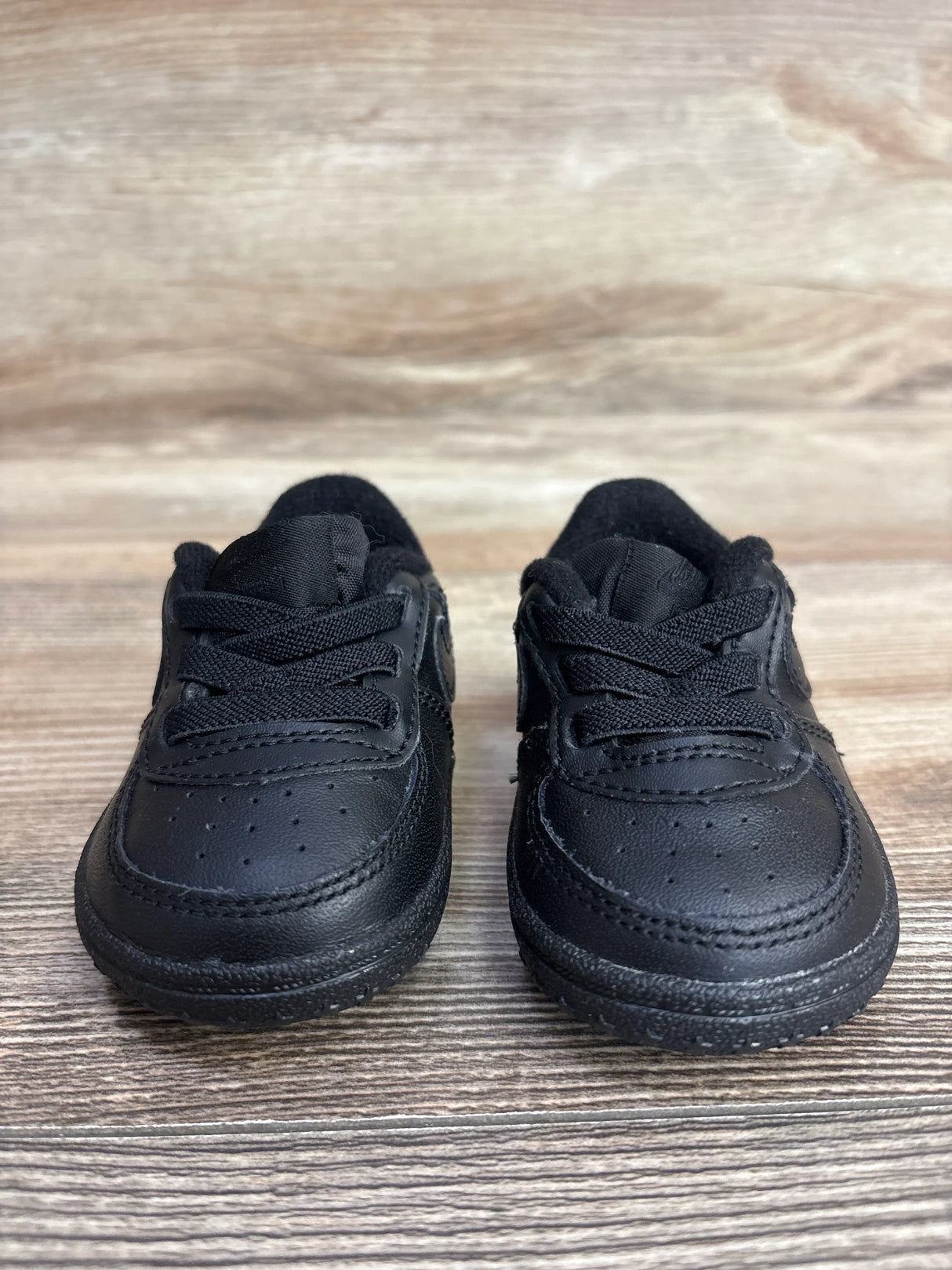 Pair of black baby sneakers with laces on a wooden surface for kids