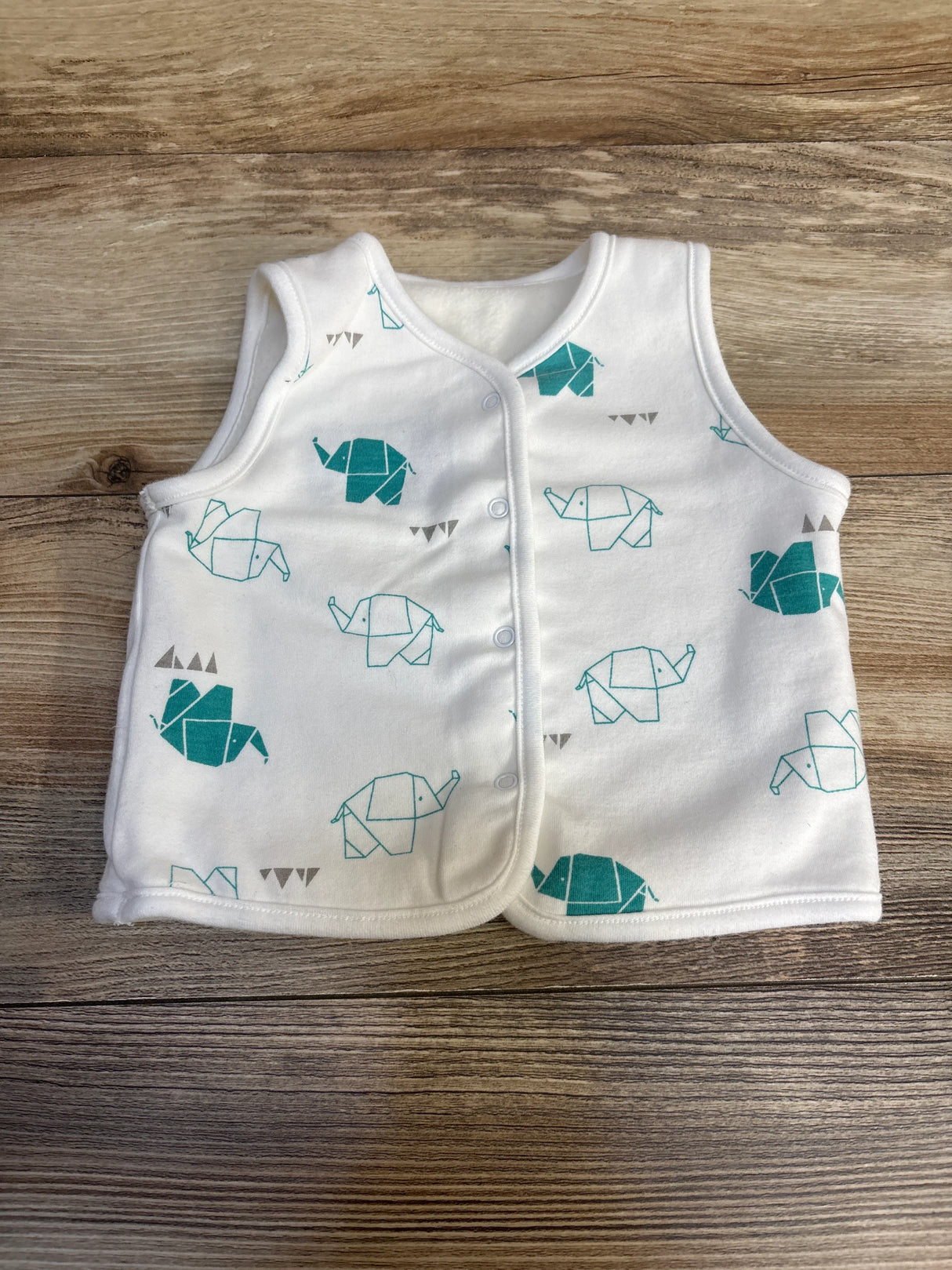 White baby vest with teal origami elephant print, sleeveless, snap buttons, on wood background