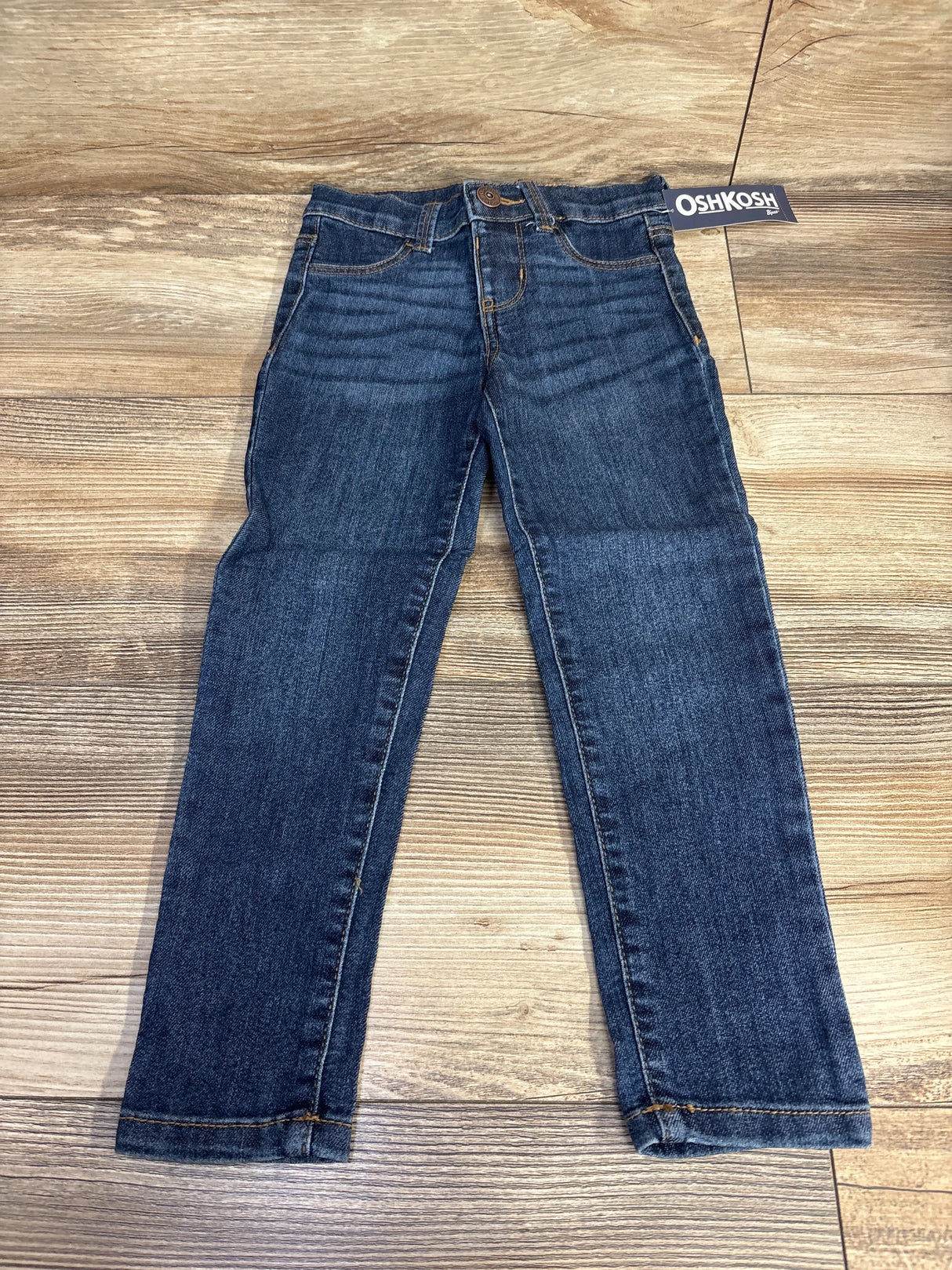 OshKosh blue denim jeans for kids laid flat on wood floor