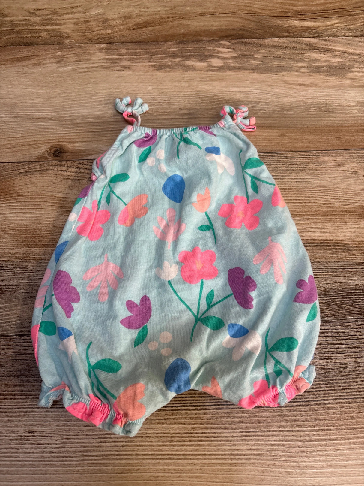 Flat lay of Carters shortie romper size 3m showcasing light blue with floral print and knotted shoulder straps on wood plank floor