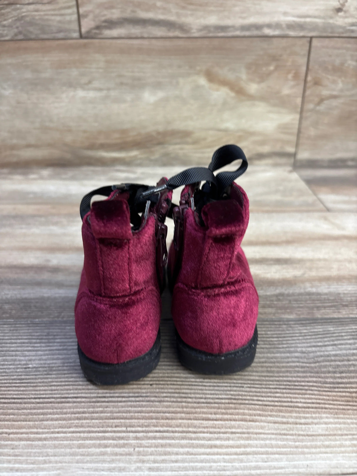 Rear view of Cat and Jack toddler velvet ankle boots in burgundy showcasing back pull tabs and side zippers on a wood-look background