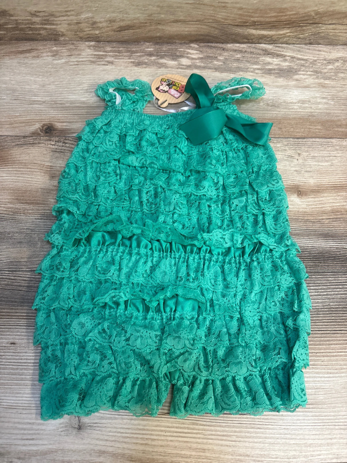 Green lace ruffle baby romper with bow detail on wooden background