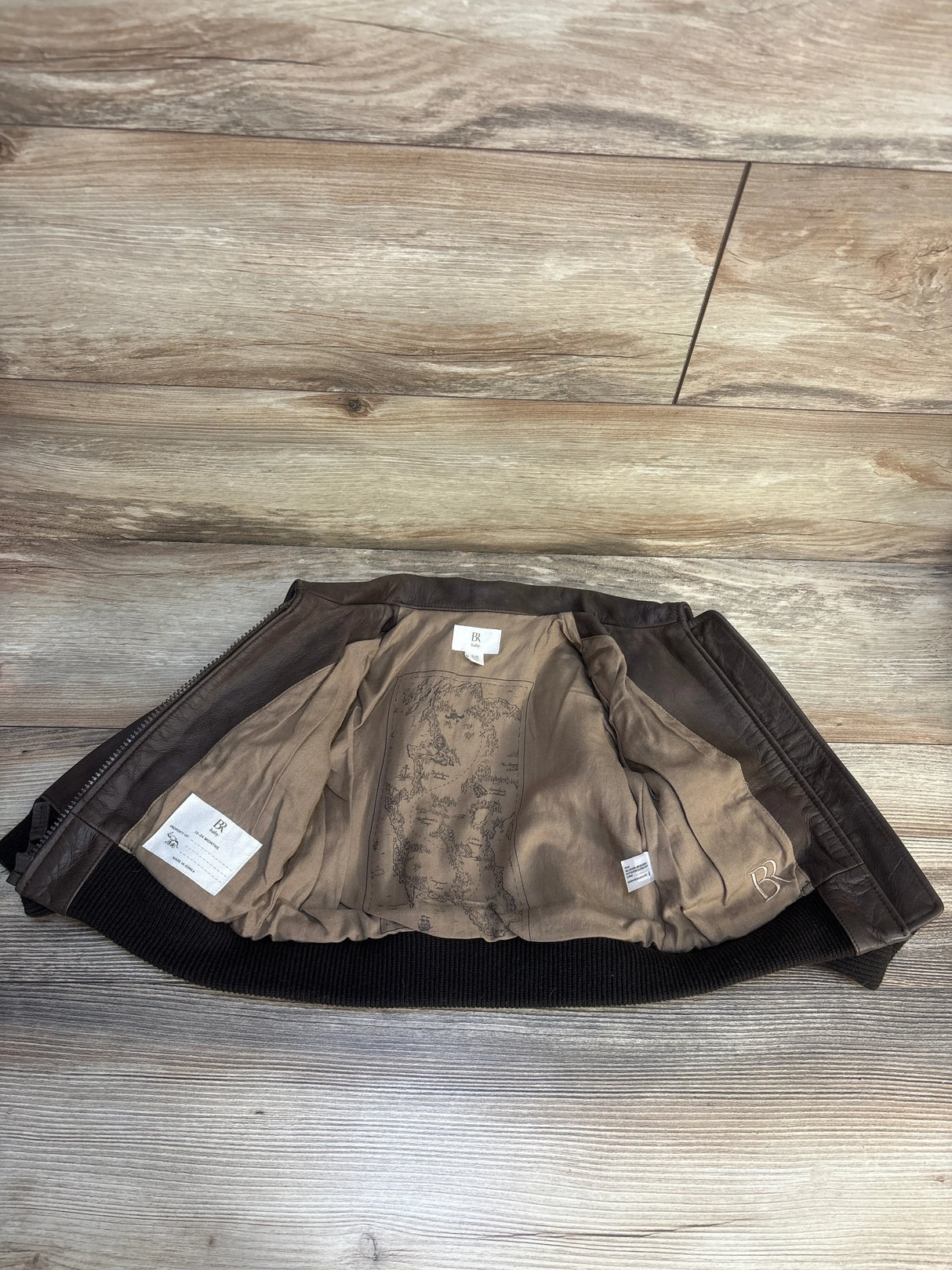 Brown leather kids jacket with tan inner lining and interior map design, laid open on wood floor