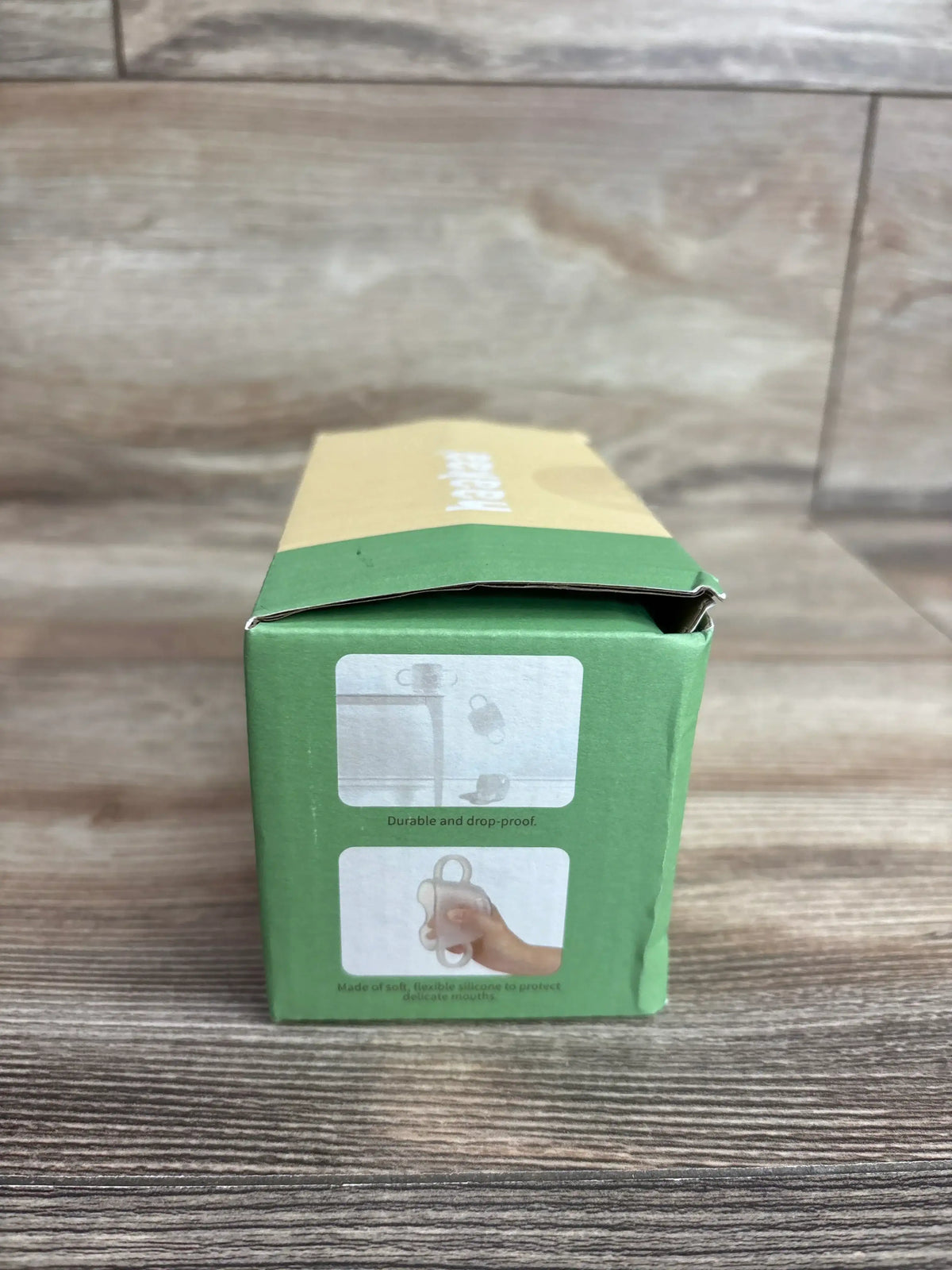 Front of Haakaa silicone baby drinking cup box showing durability icons and green-yellow packaging on wooden tabletop