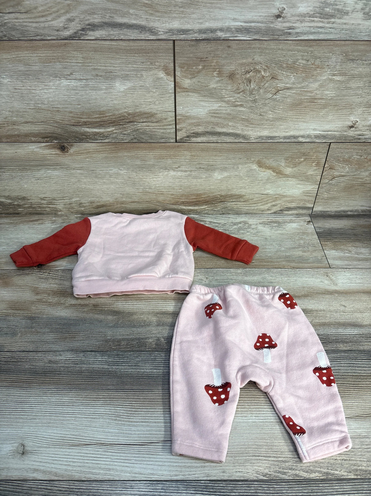 Pink baby outfit with red sleeves and matching pants featuring red mushroom prints on wood floor