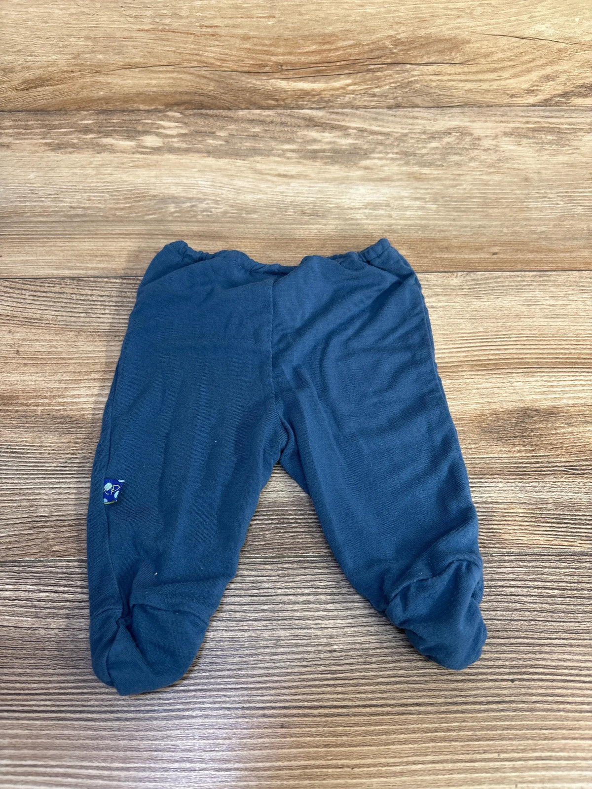 Top view of Kickee Pants bamboo footed pants in blue showcasing enclosed feet and elastic waistband on a wood-grain background