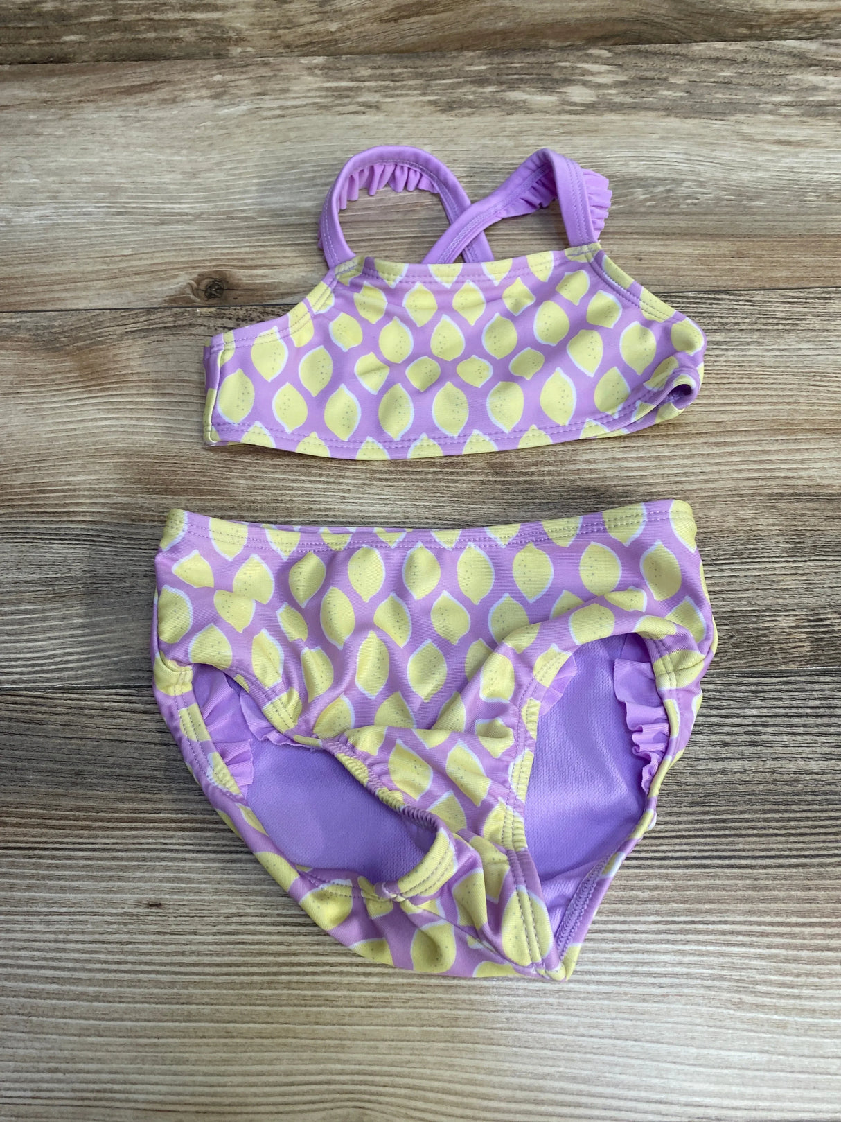 Flat lay of Cat and Jack two-piece toddler swimsuit in purple with yellow lemon print, ruffled straps on wood background