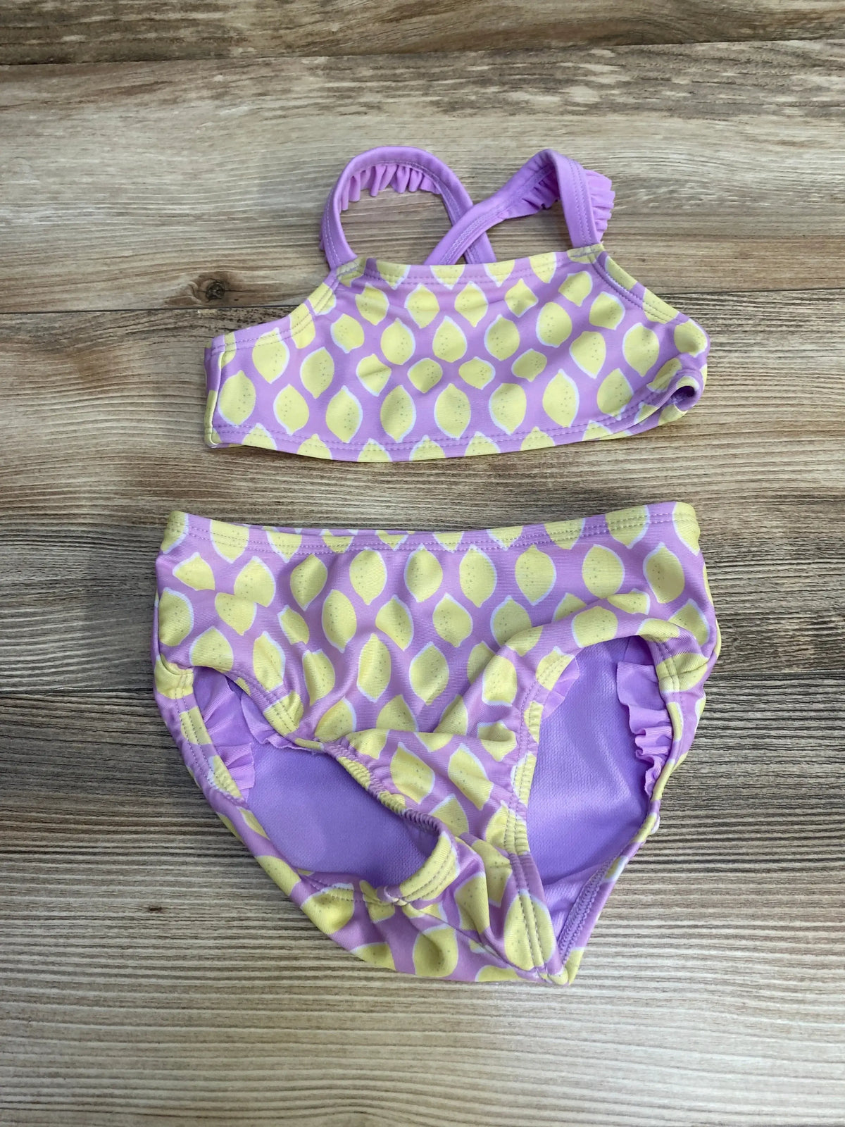 Flat lay of Cat and Jack two-piece toddler swimsuit in purple with yellow lemon print, ruffled straps on wood background