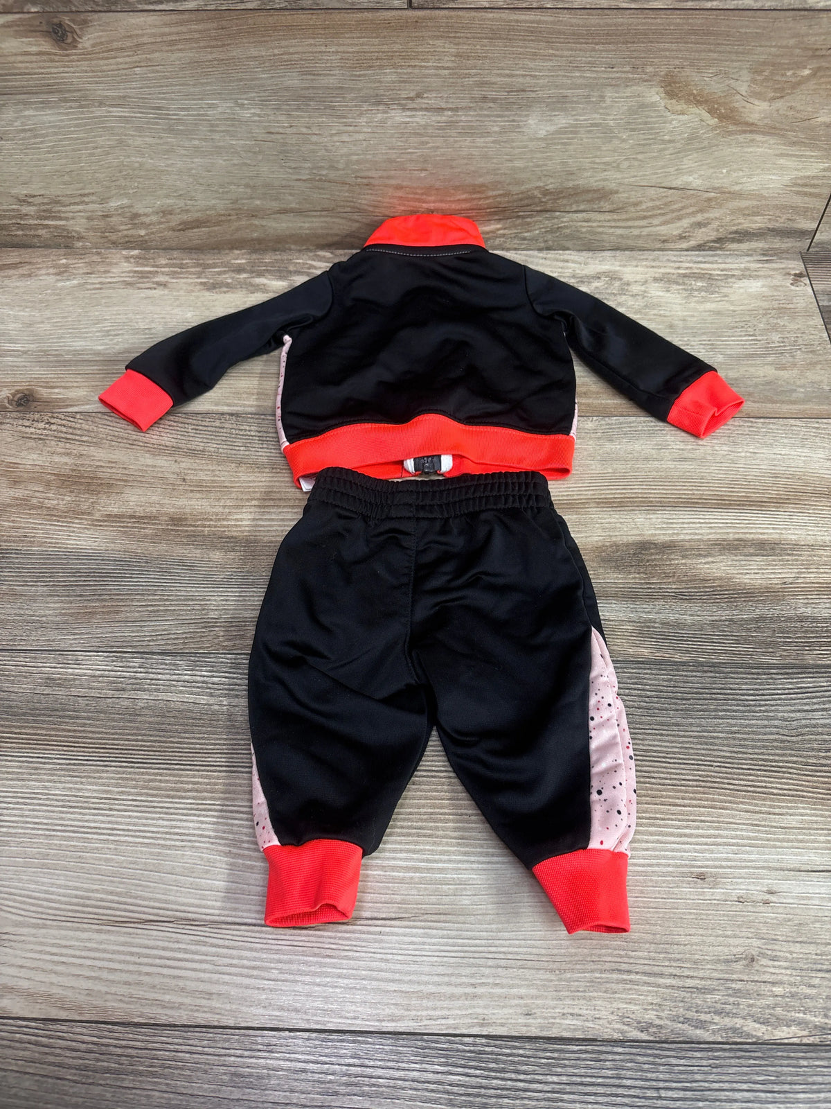 Flat lay of Jordan 2pc tracksuit for newborns, black and red with pink patterned pant panels, on a wood floor