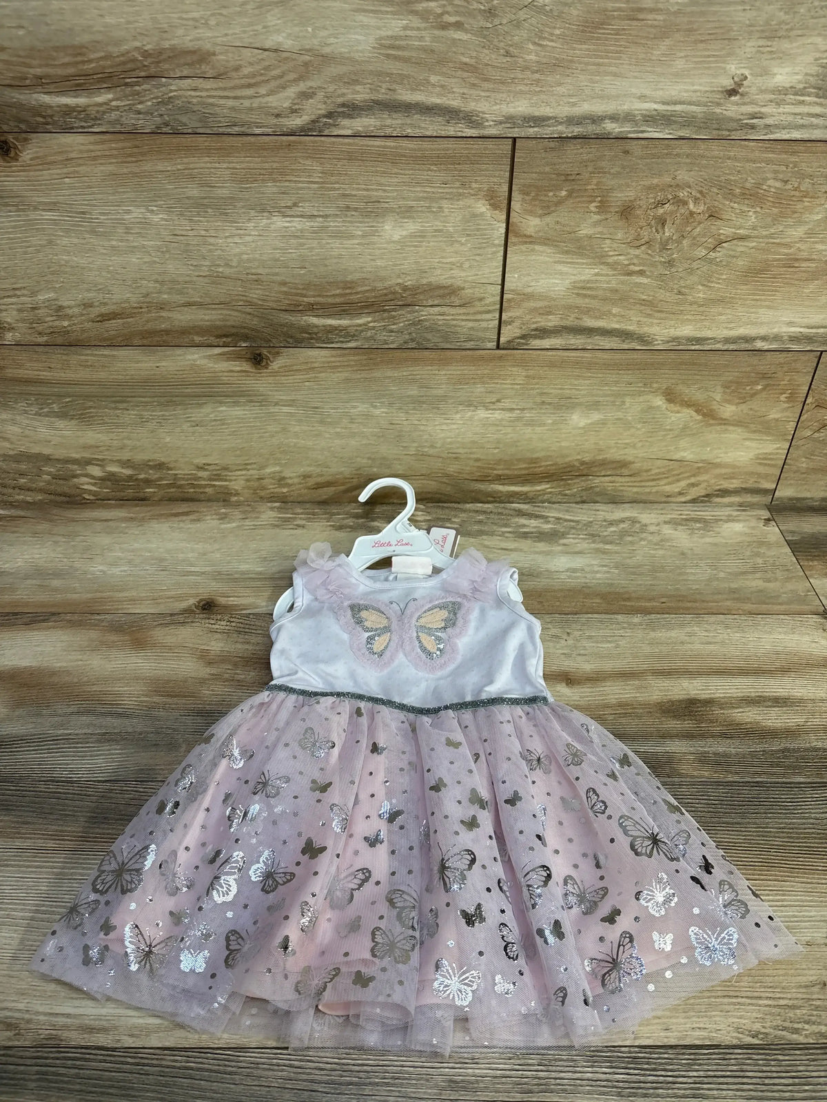 Front view of new Little Lass lilac butterfly dress on hanger with metallic butterfly tulle skirt against wood plank wall