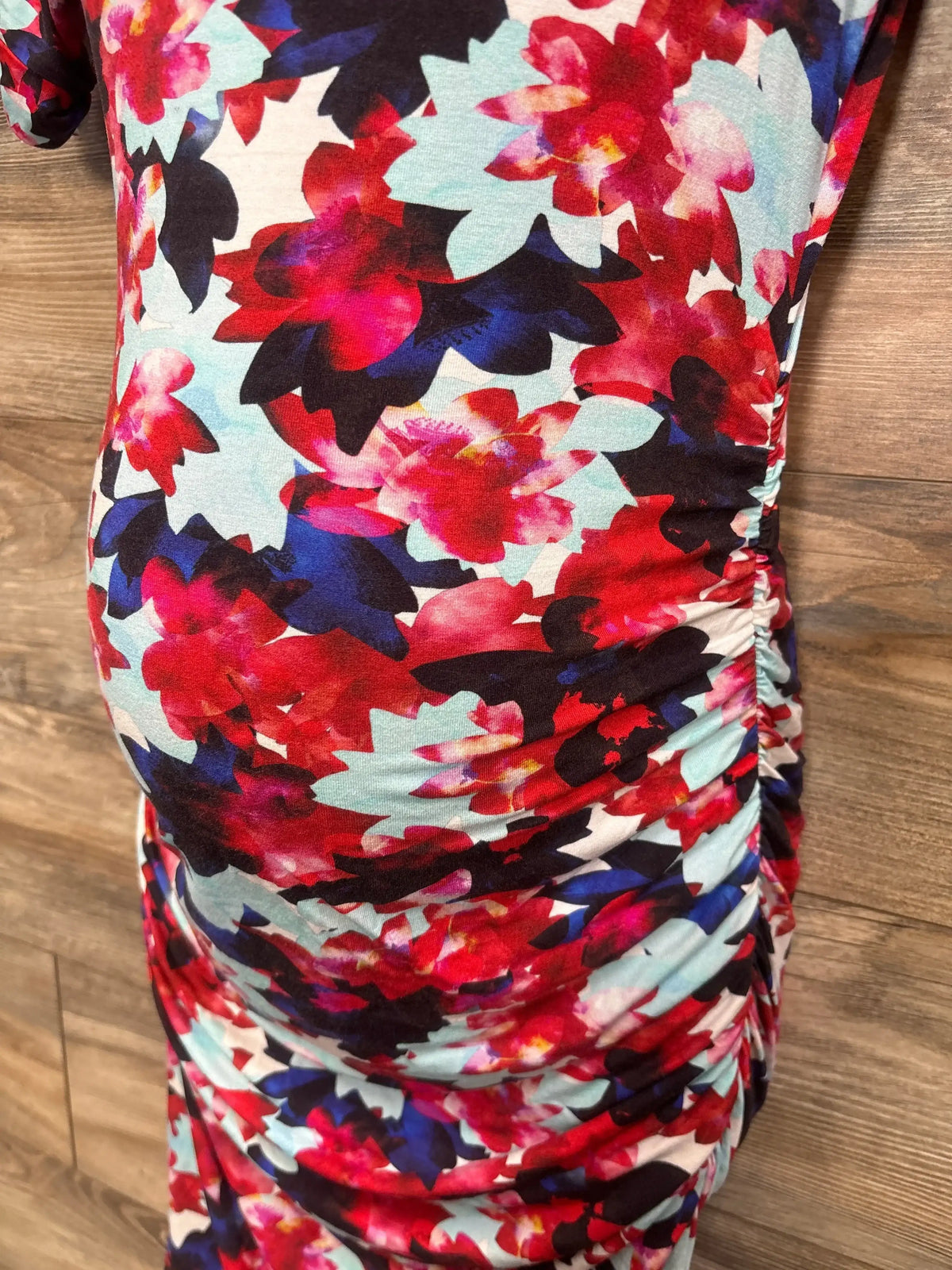 Close-up of red floral bodycon maternity dress showcasing ruched sides on a wood floor