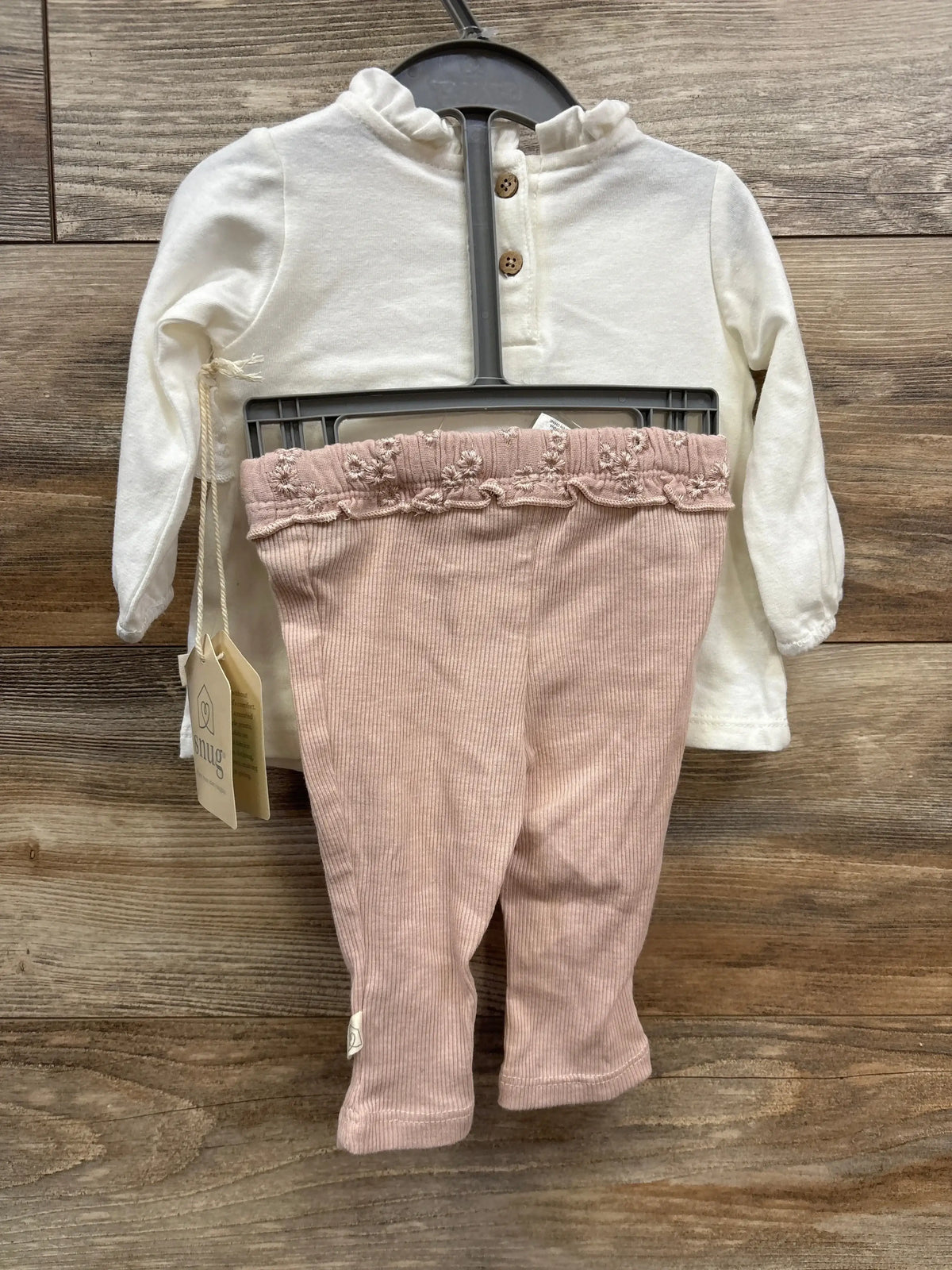 Baby girl's outfit with cream ruffled collar top and pink embroidered ruffle leggings on wooden floor