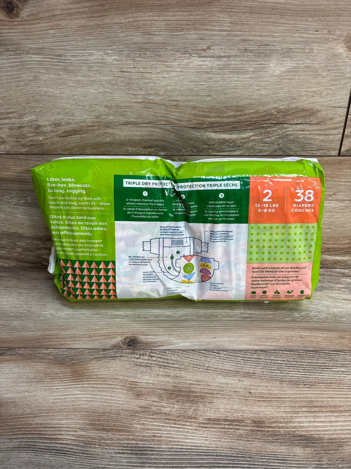 Rear view of Babyganics diapers size 2 pack showing Triple Dry Protection diagram and orange size panel on wooden tabletop