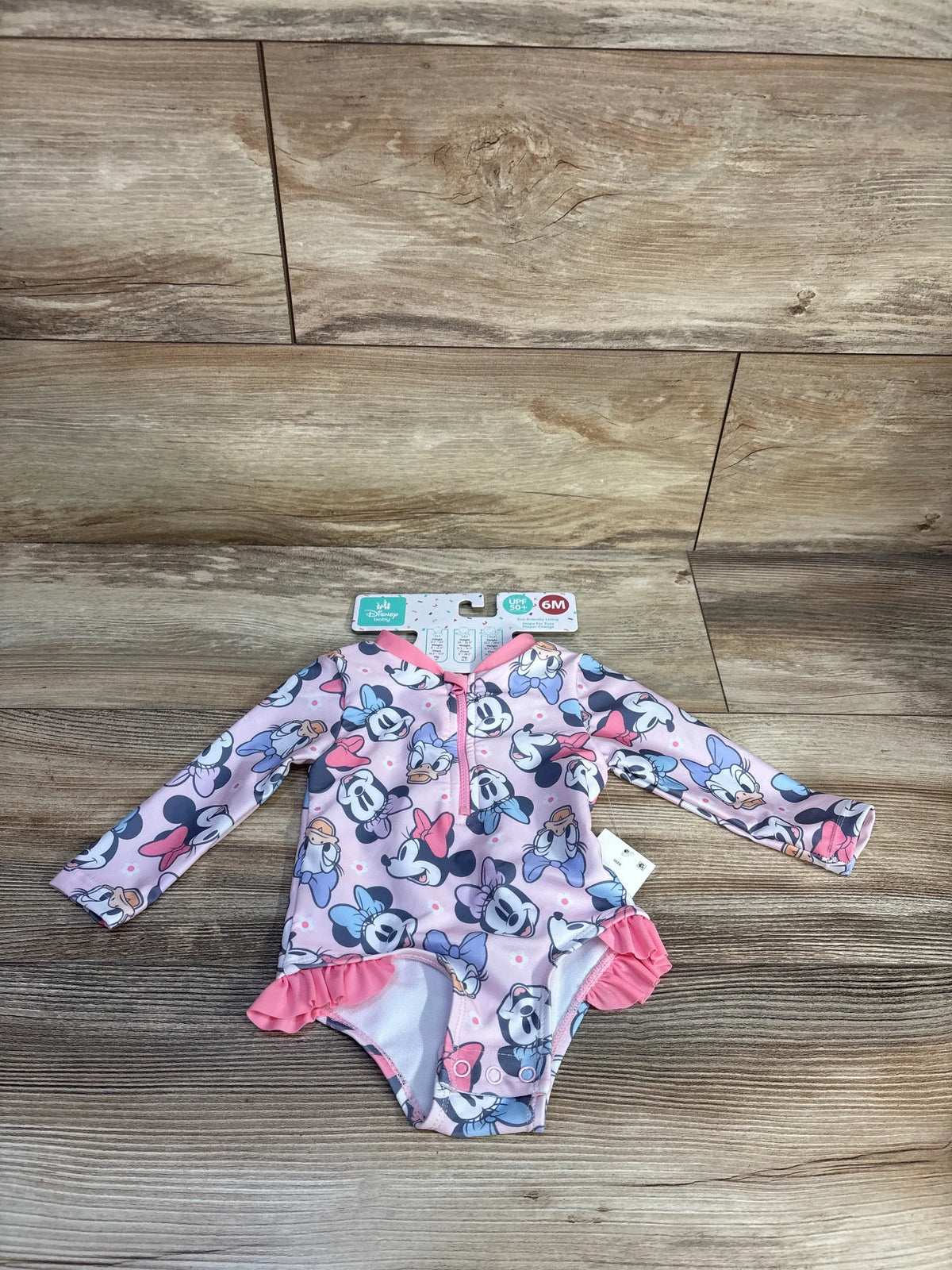 Flat lay of pink Disney Baby Minnie Mouse one-piece rash guard swimsuit with long sleeves, ruffles, and UPF 50+ tag