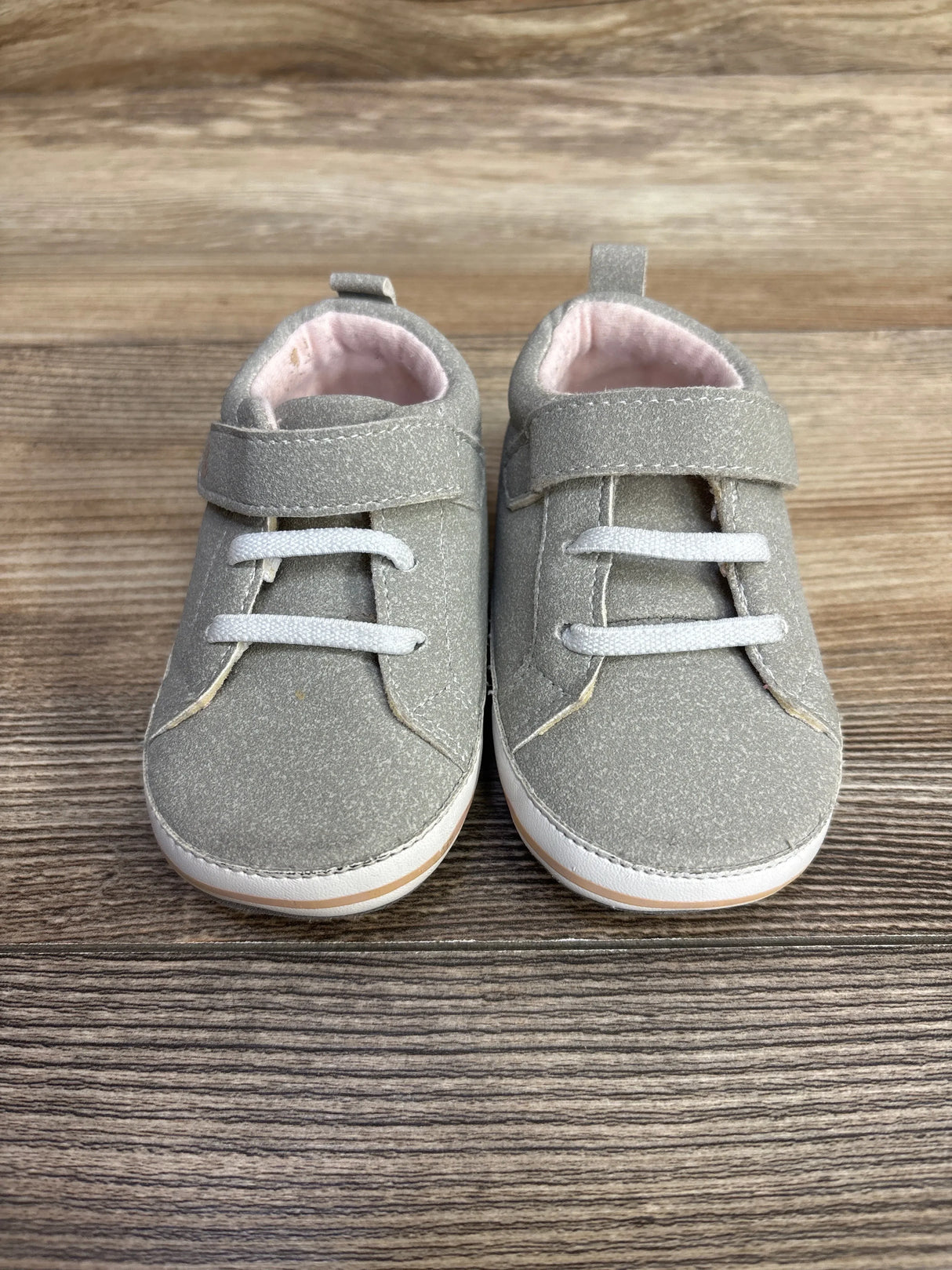 Pair of gray baby shoes with white laces and pink lining on wooden floor
