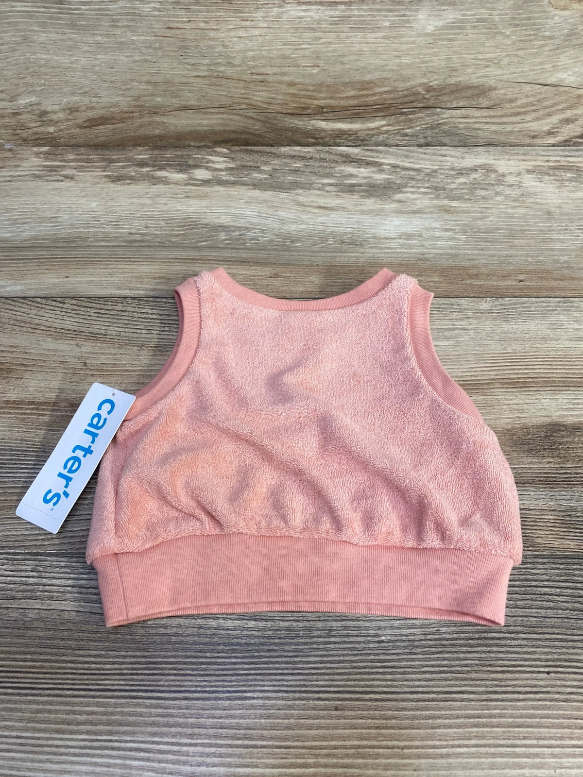 Top-down view of pink terry cloth baby tank top showing ribbed hem, sleeveless armholes, and scoop neckline on a wood-plank background